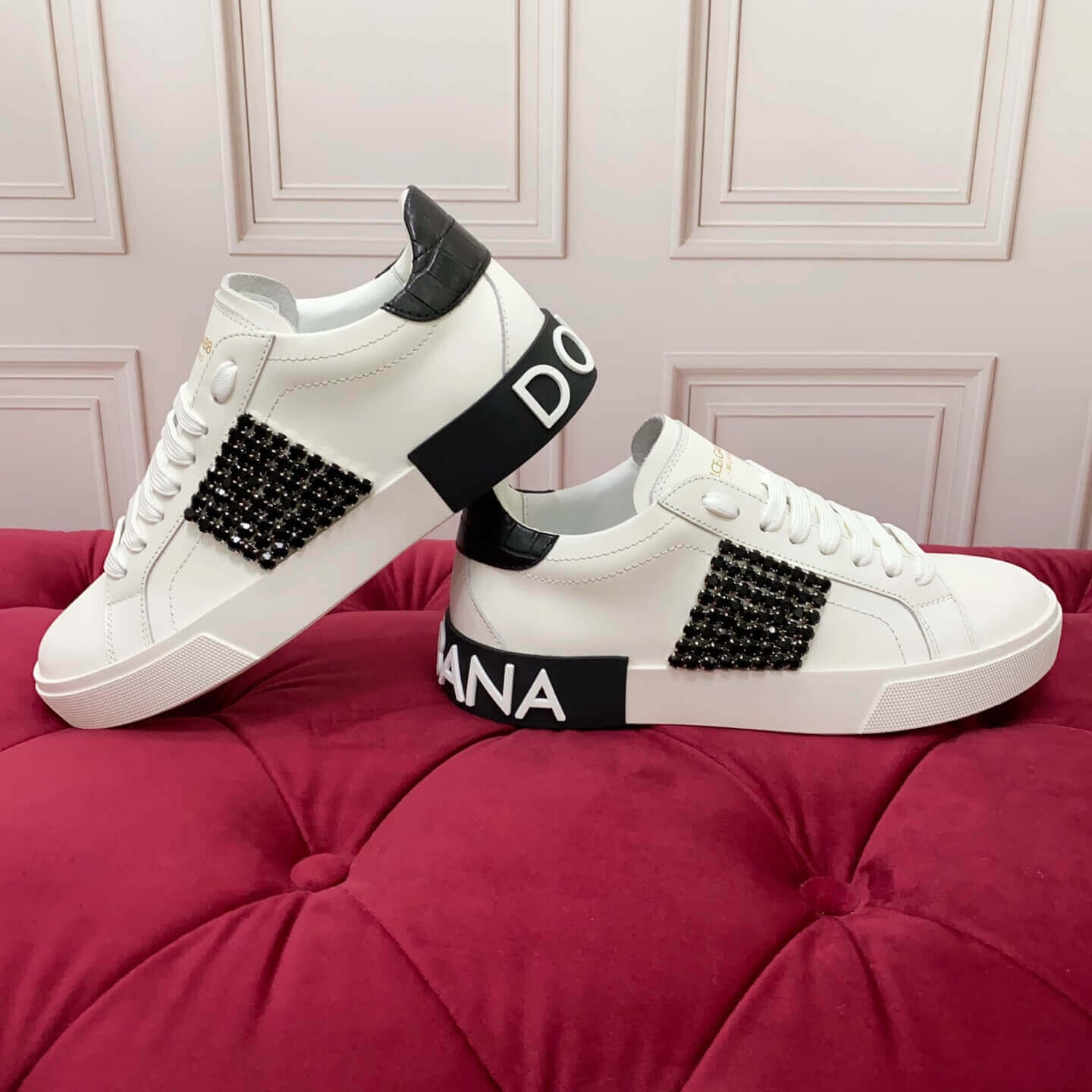 White Dolce & Gabbana sneakers Dolce & Gabbana Women Calfskin Portofino Vintage Sneakers with Black Crystal Embellishment - White & Black Product Description, displayed on a red cushioned surface