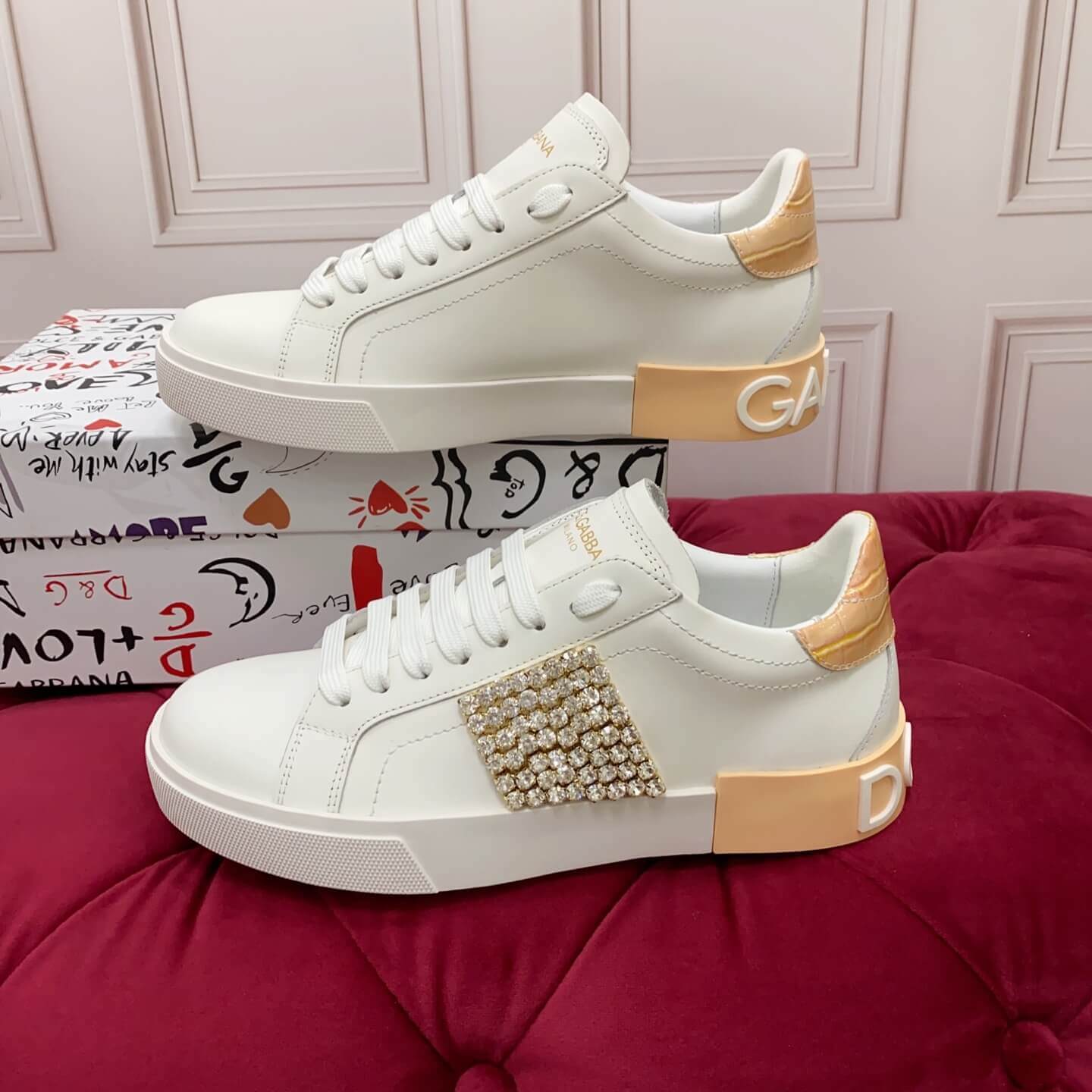 Dolce & Gabbana Women's Portofino Sneakers with Crystal Embellishment & Vintage Logo Heel - White, displayed on a red cushioned surface