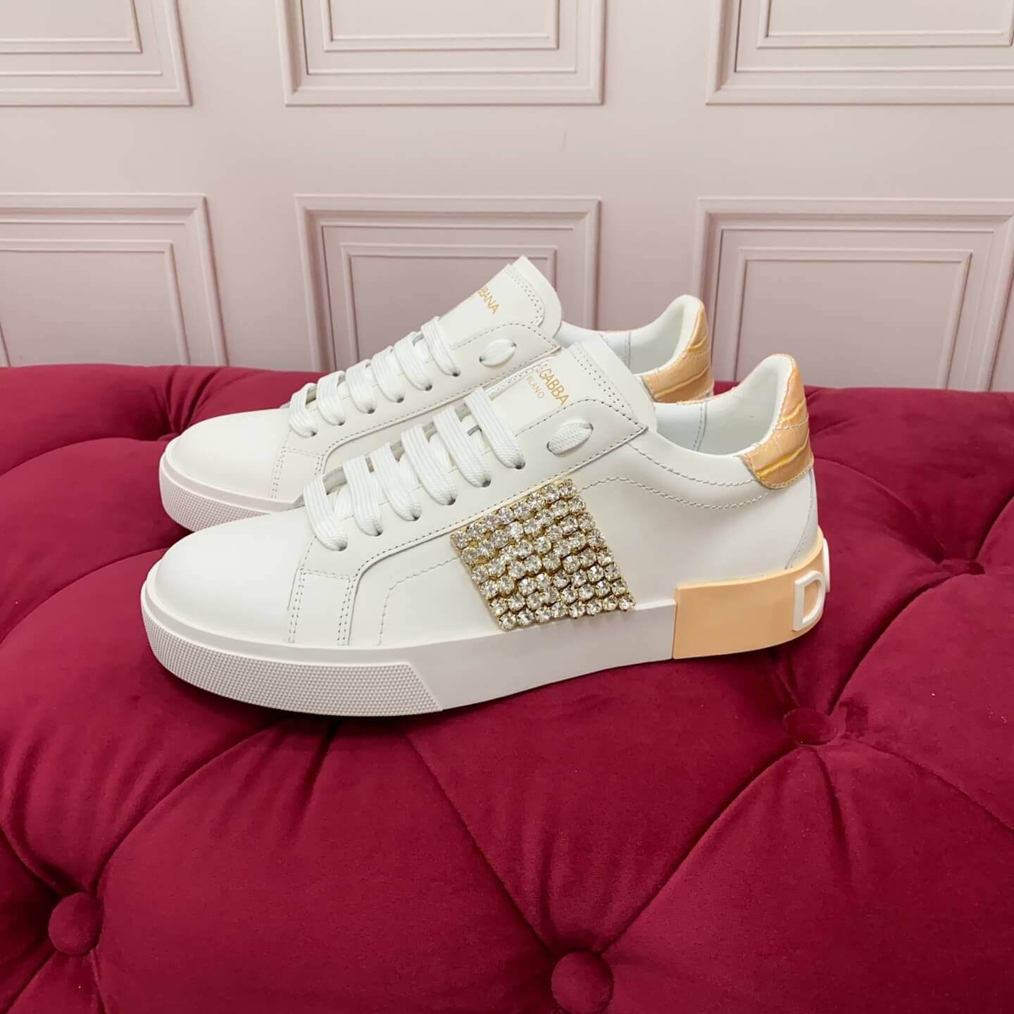 Dolce & Gabbana Women's Portofino Sneakers with Crystal Embellishment & Vintage Logo Heel - White, displayed on a red cushioned surface