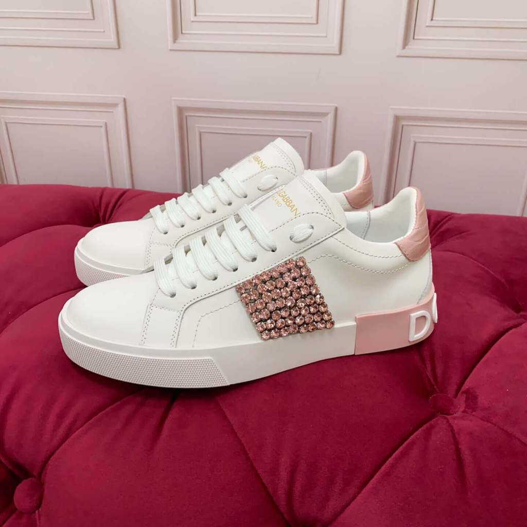Dolce & Gabbana Women's Portofino Sneakers with Pink Crystal Embellishment & Pink Heel - White, displayed on a red cushioned surface