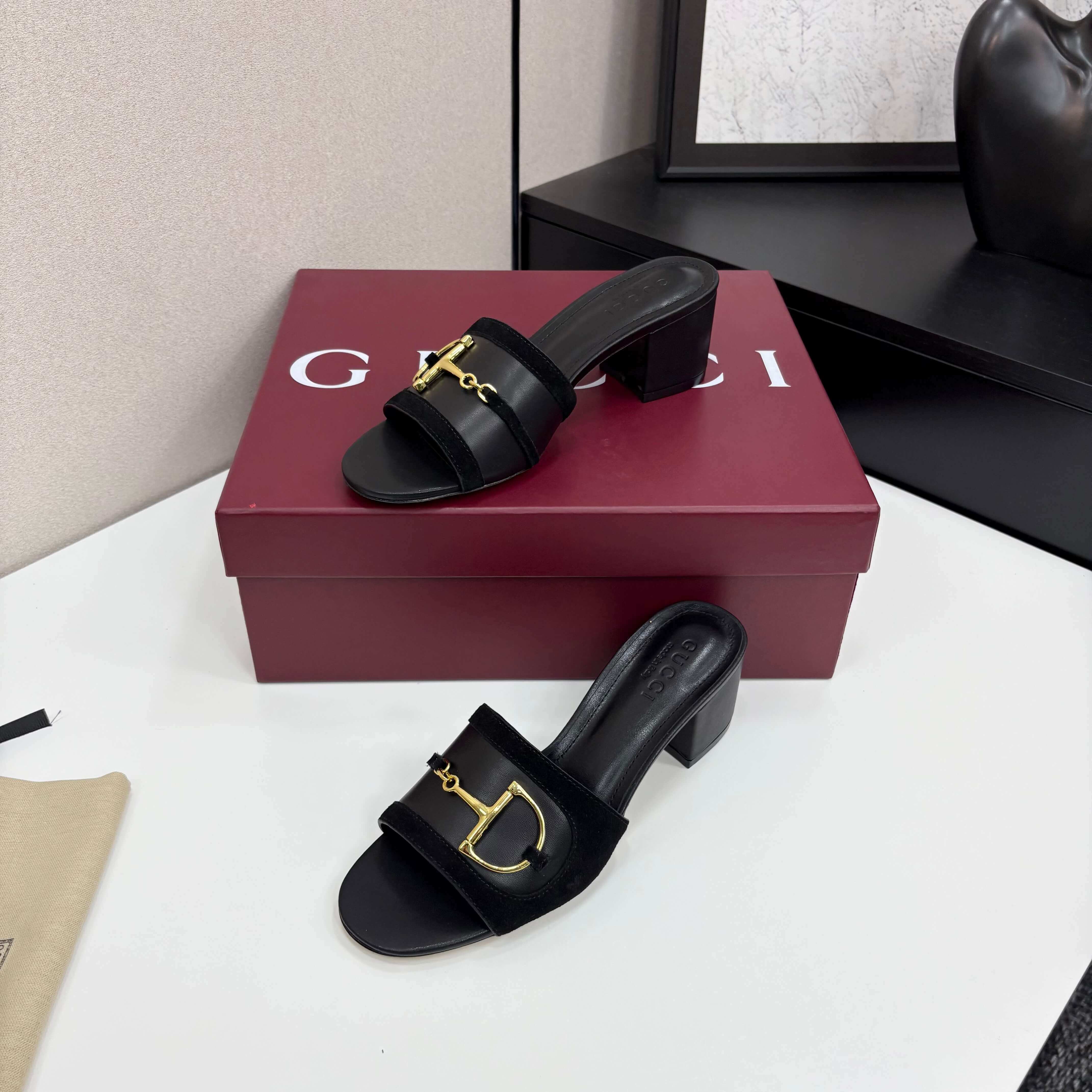 a pair of Gucci Women's Black Suede Block Heel Slide Sandals with Horsebit and GG Monogram Canvas on a red box