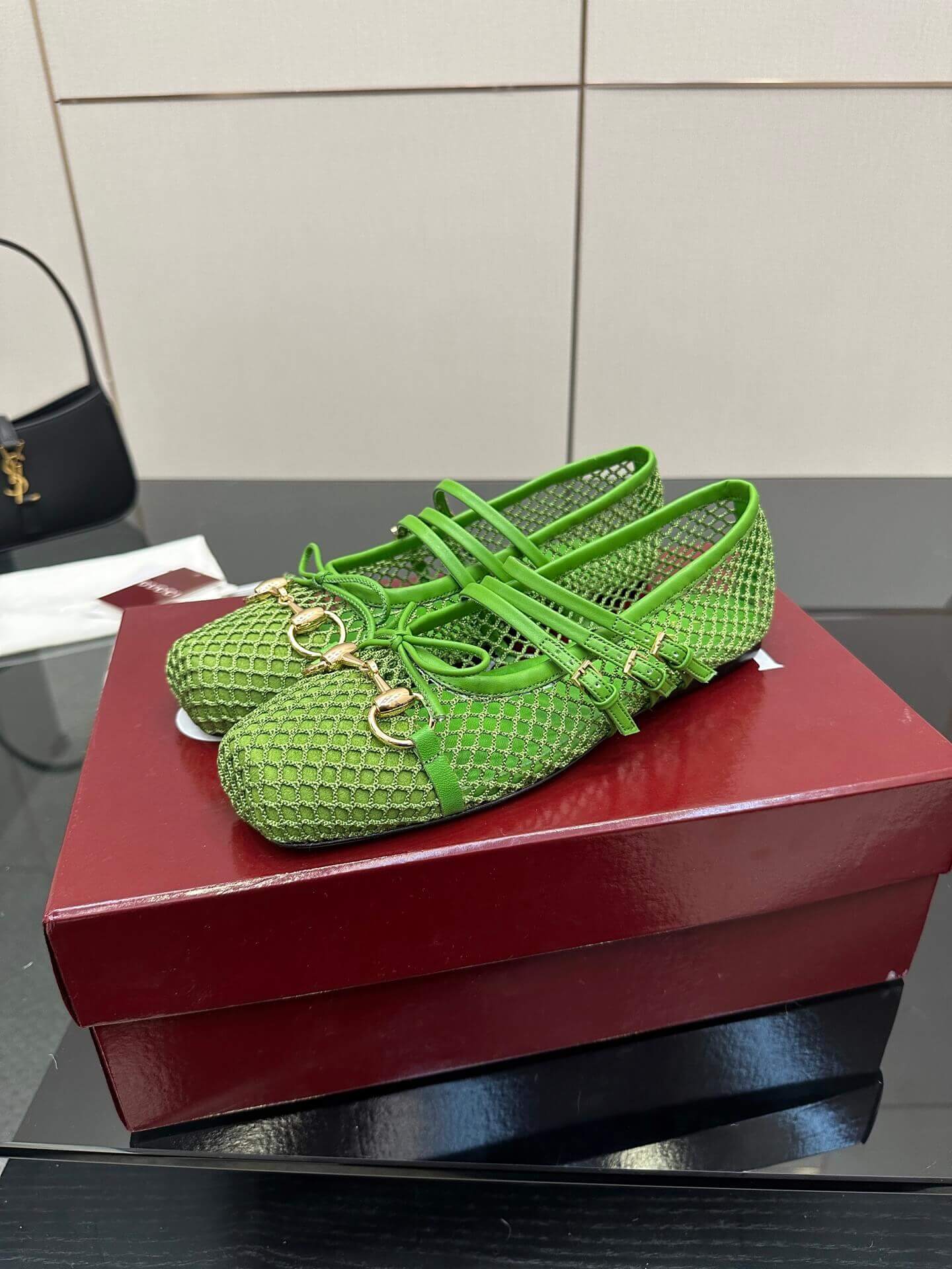 a pair of Gucci Women's Horsebit Ballet Flat - Green Mesh on a red box on a glass table