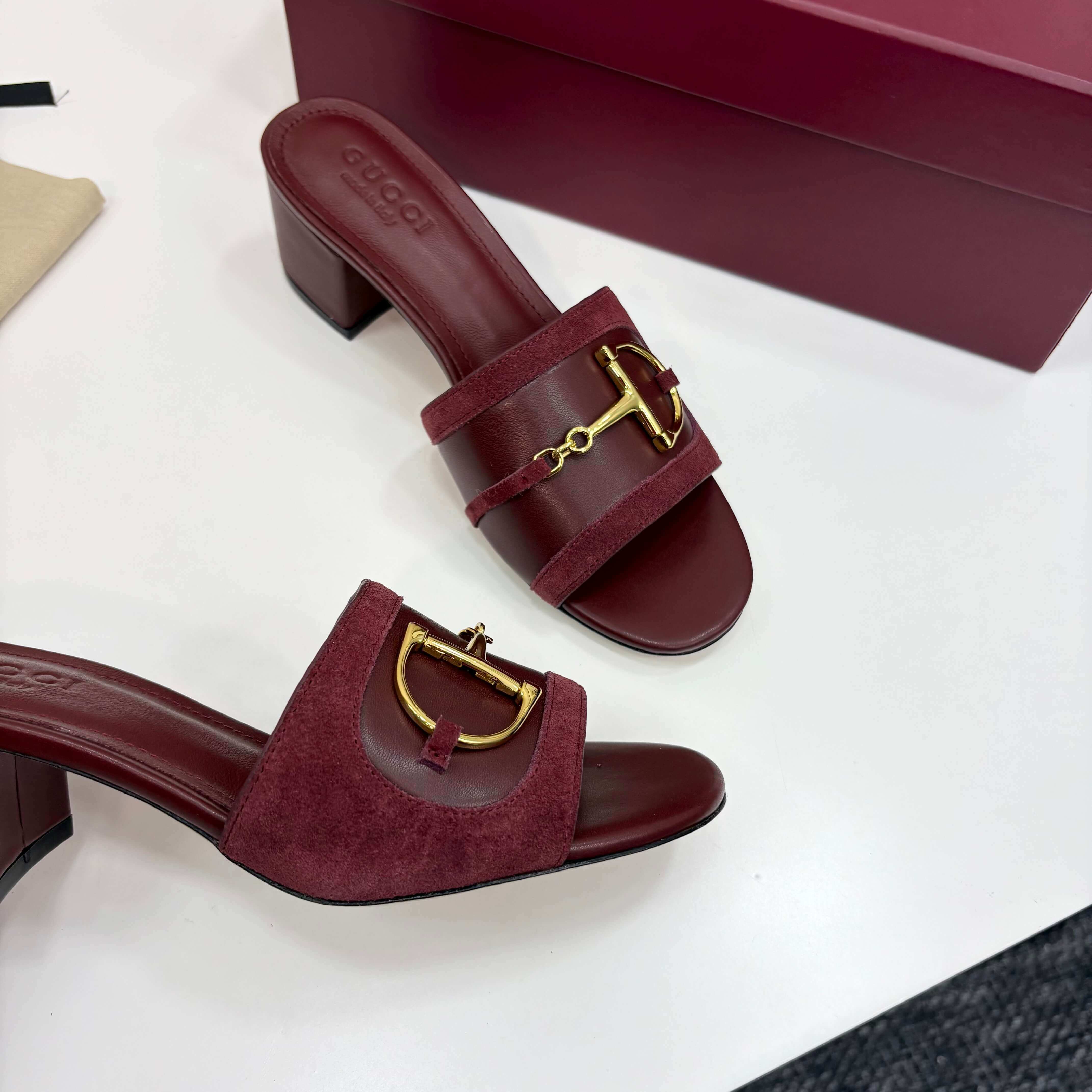 a pair of Gucci Women's Rosso Ancora Red Suede Block Heel Slide Sandals with Horsebit on a white
