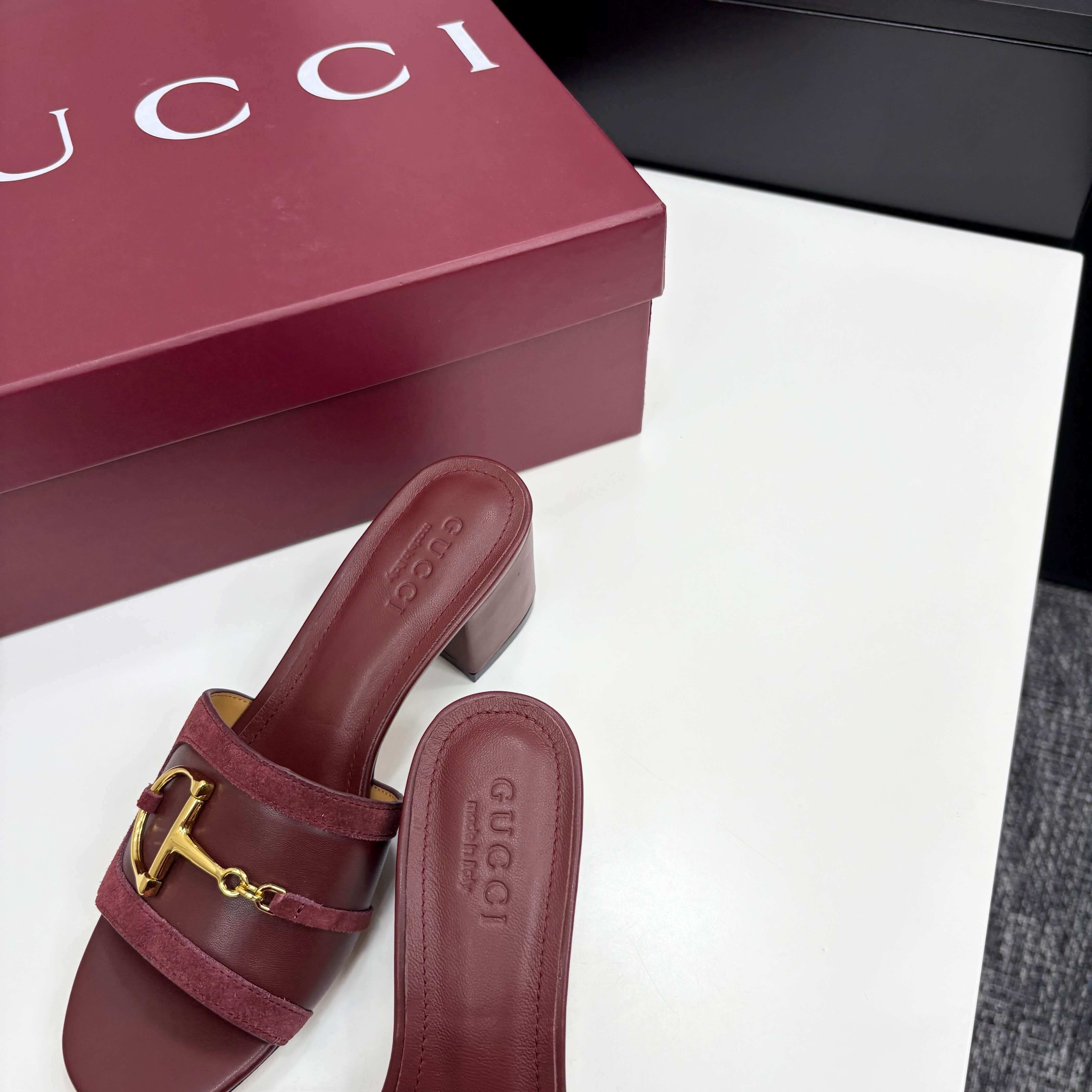 a pair of Gucci Women's Rosso Ancora Red Suede Block Heel Slide Sandals with Horsebit on a white