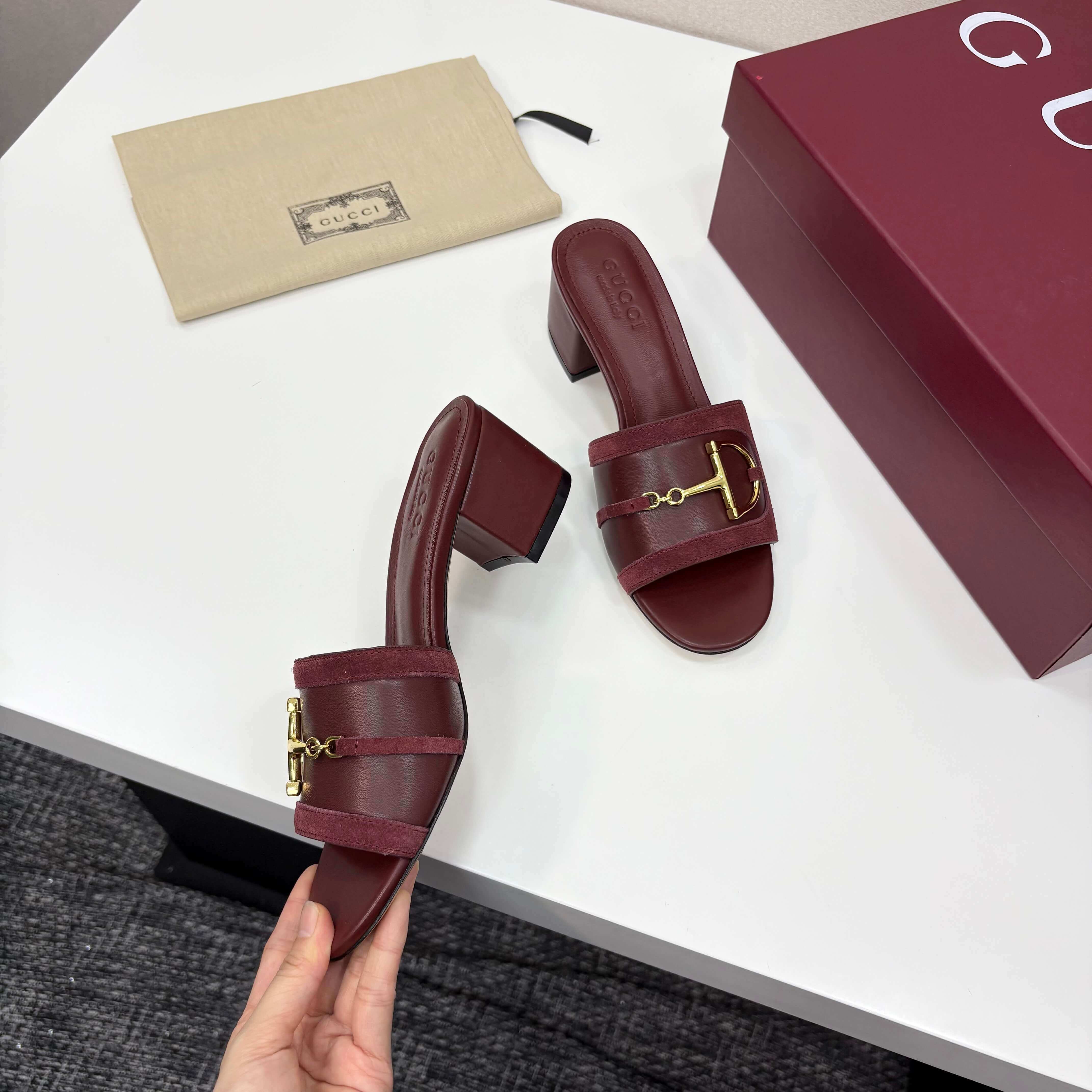 a pair of Gucci Women's Rosso Ancora Red Suede Block Heel Slide Sandals with Horsebit on a white