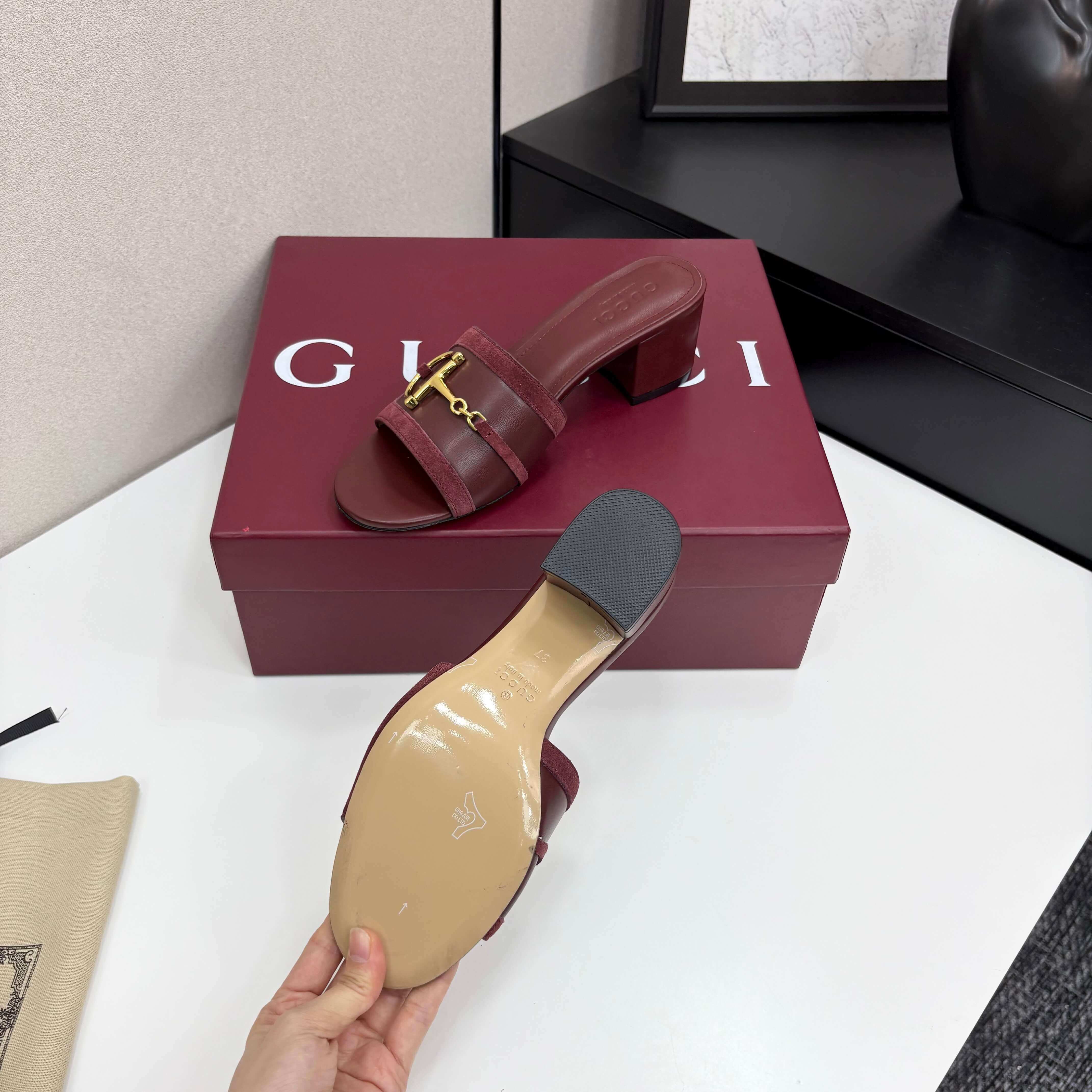 a pair of Gucci Women's Rosso Ancora Red Suede Block Heel Slide Sandals with Horsebit on a white