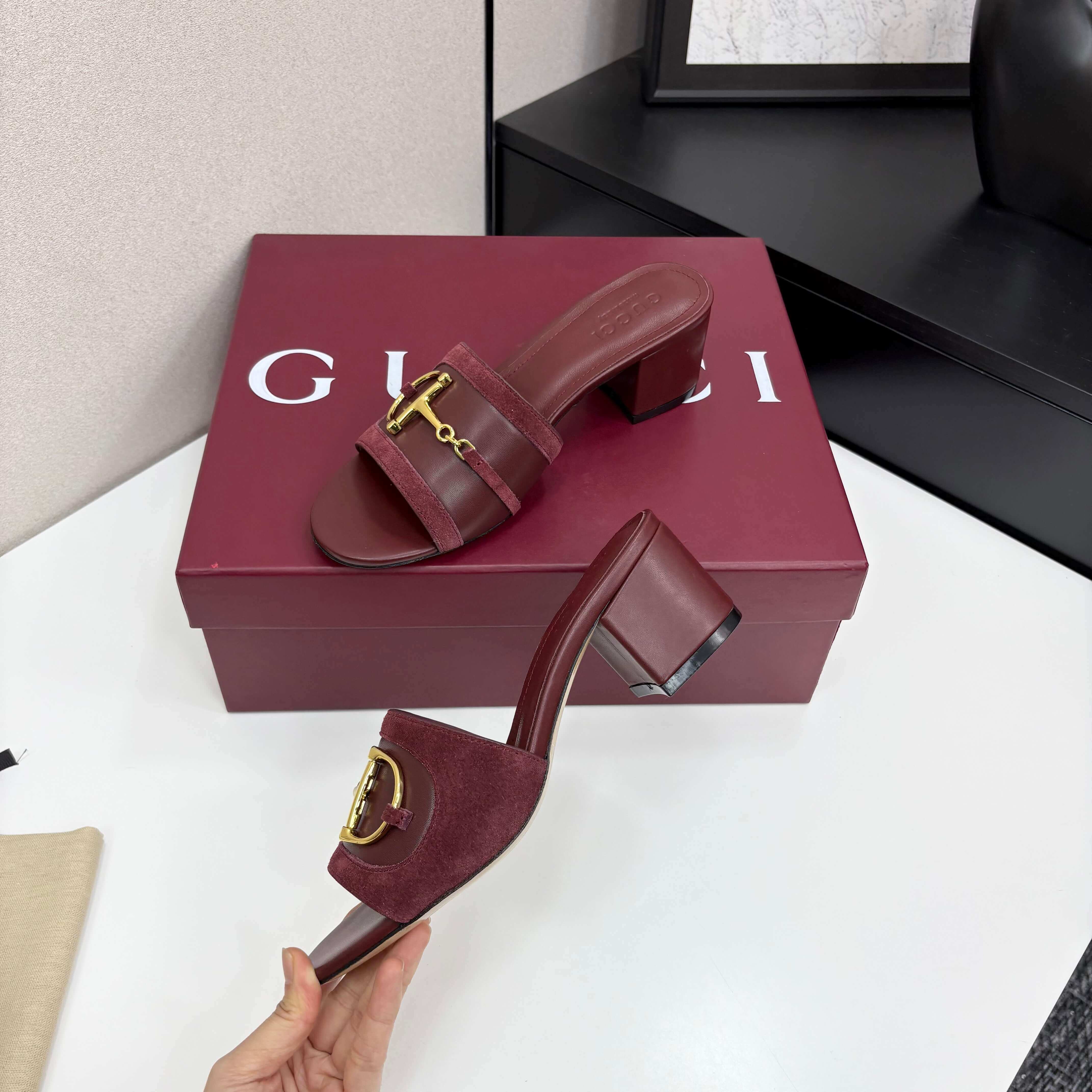 a pair of Gucci Women's Rosso Ancora Red Suede Block Heel Slide Sandals with Horsebit on a white