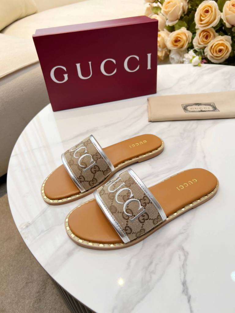 a pair of Gucci Women's Tan Leather Slide Sandals with Silver-Toned GG Monogram and Silver Trim on a table