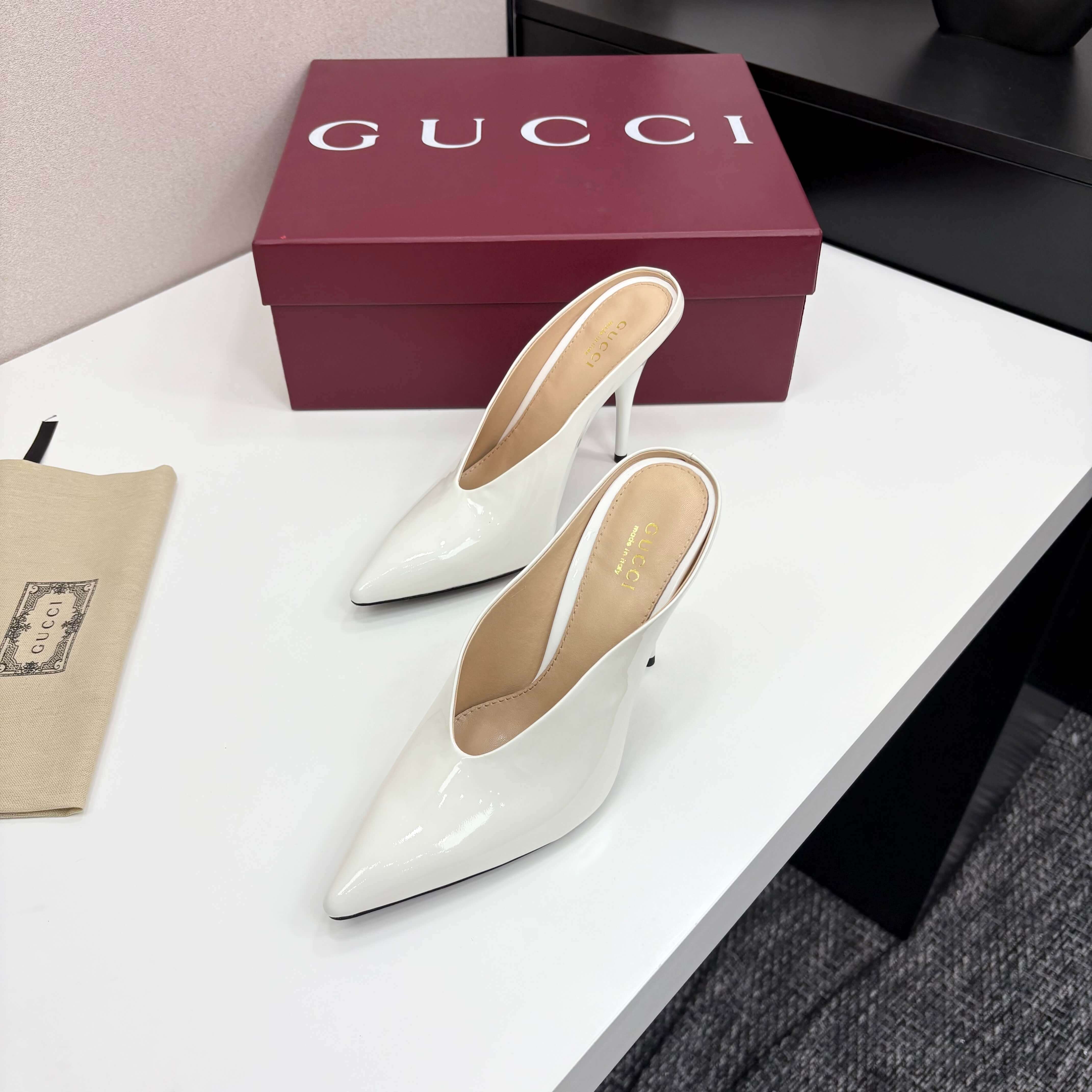 a pair of Gucci Women's White Shiny Patent Leather Pointed-Toe Stiletto Pumps on a white table