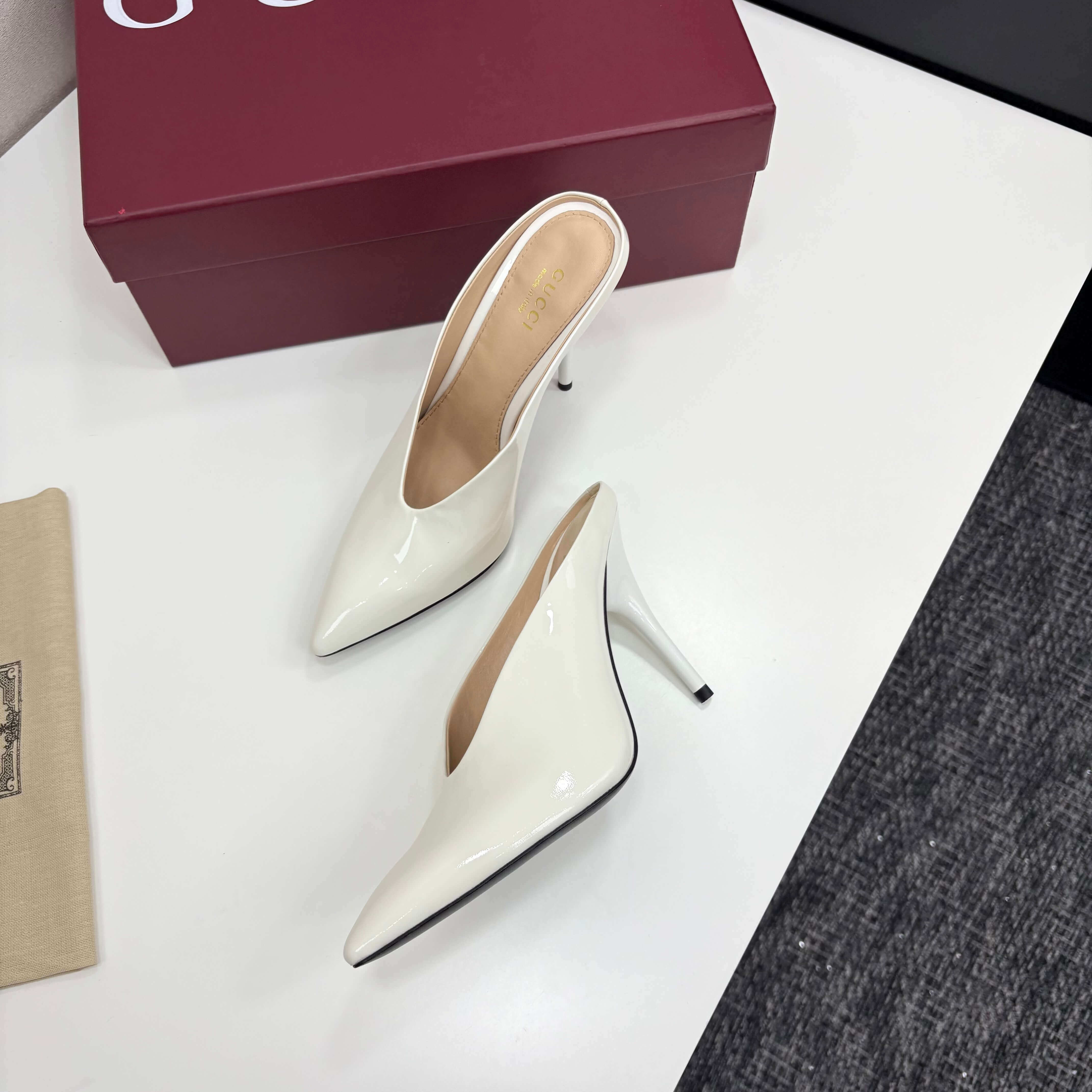 a pair of Gucci Women's White Shiny Patent Leather Pointed-Toe Stiletto Pumps on a white table