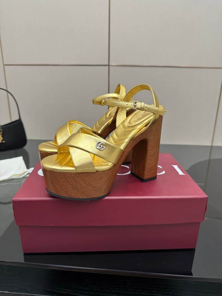 a pair of Gucci Womens platform sandal - Gold with Wooden Heel and Interlocking G Detail on a red box