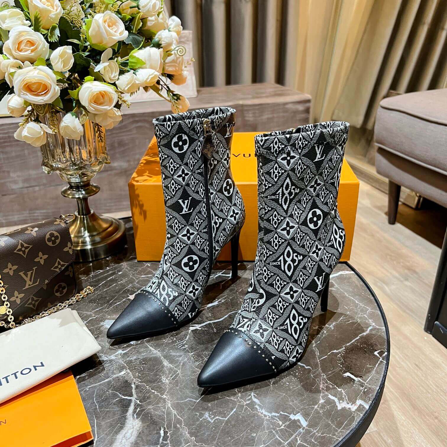 a pair of Louis Vuitton-Inspired Cherrie Ankle Boots – Monogram Noir on a table