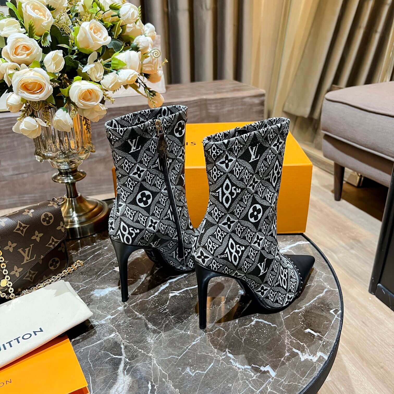 a pair of Louis Vuitton-Inspired Cherrie Ankle Boots – Monogram Noir on a table