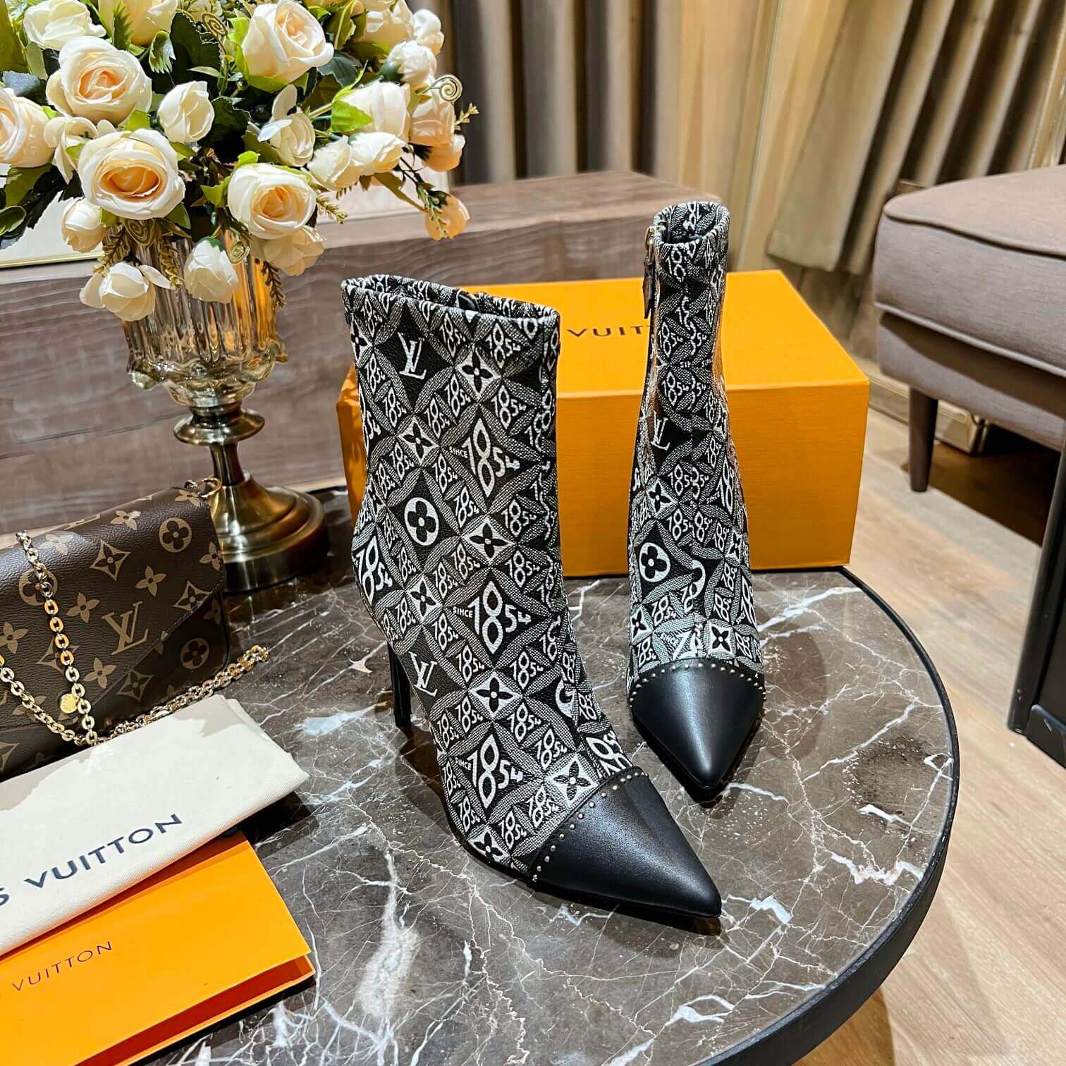 a pair of Louis Vuitton-Inspired Cherrie Ankle Boots – Monogram Noir on a table