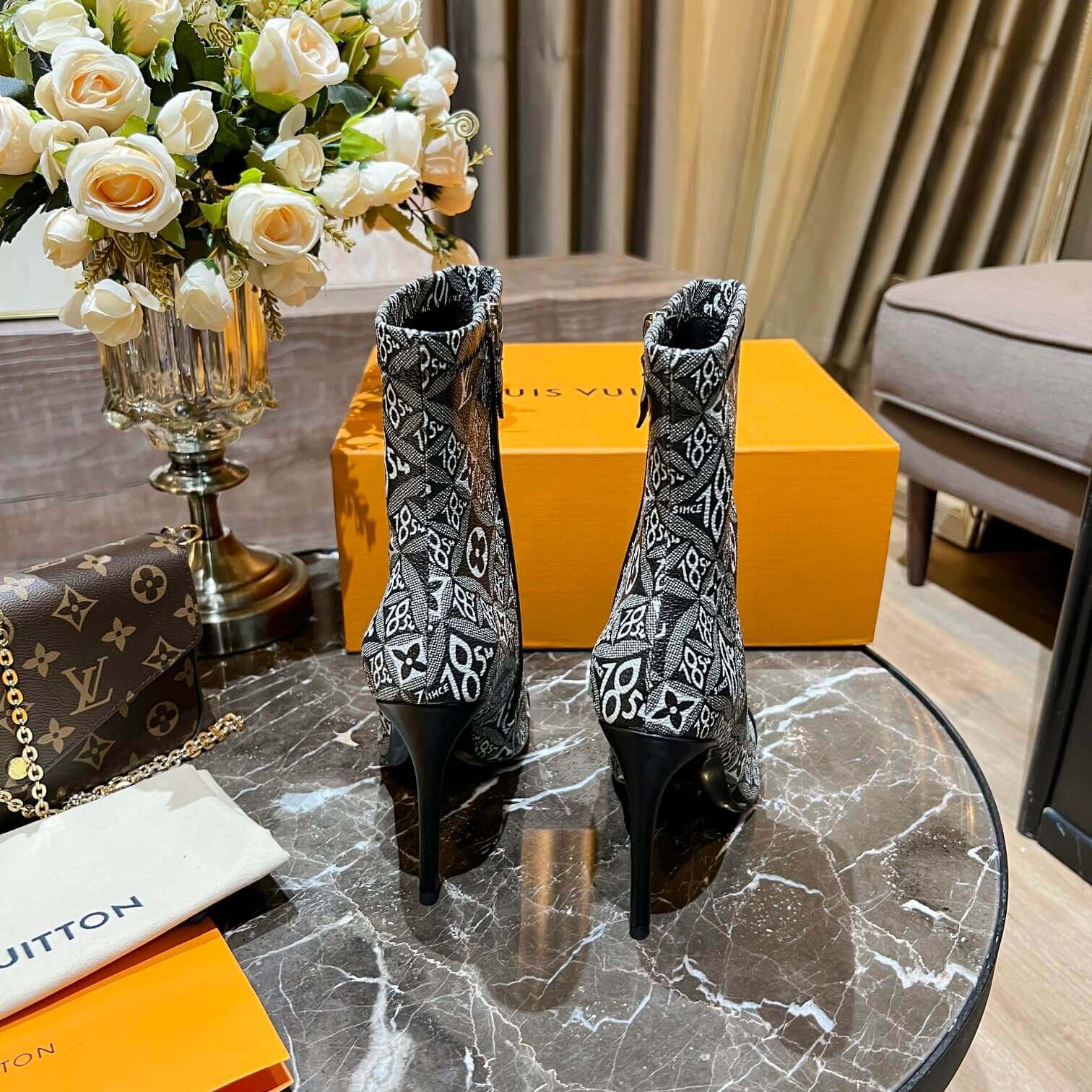 a pair of Louis Vuitton-Inspired Cherrie Ankle Boots – Monogram Noir on a table