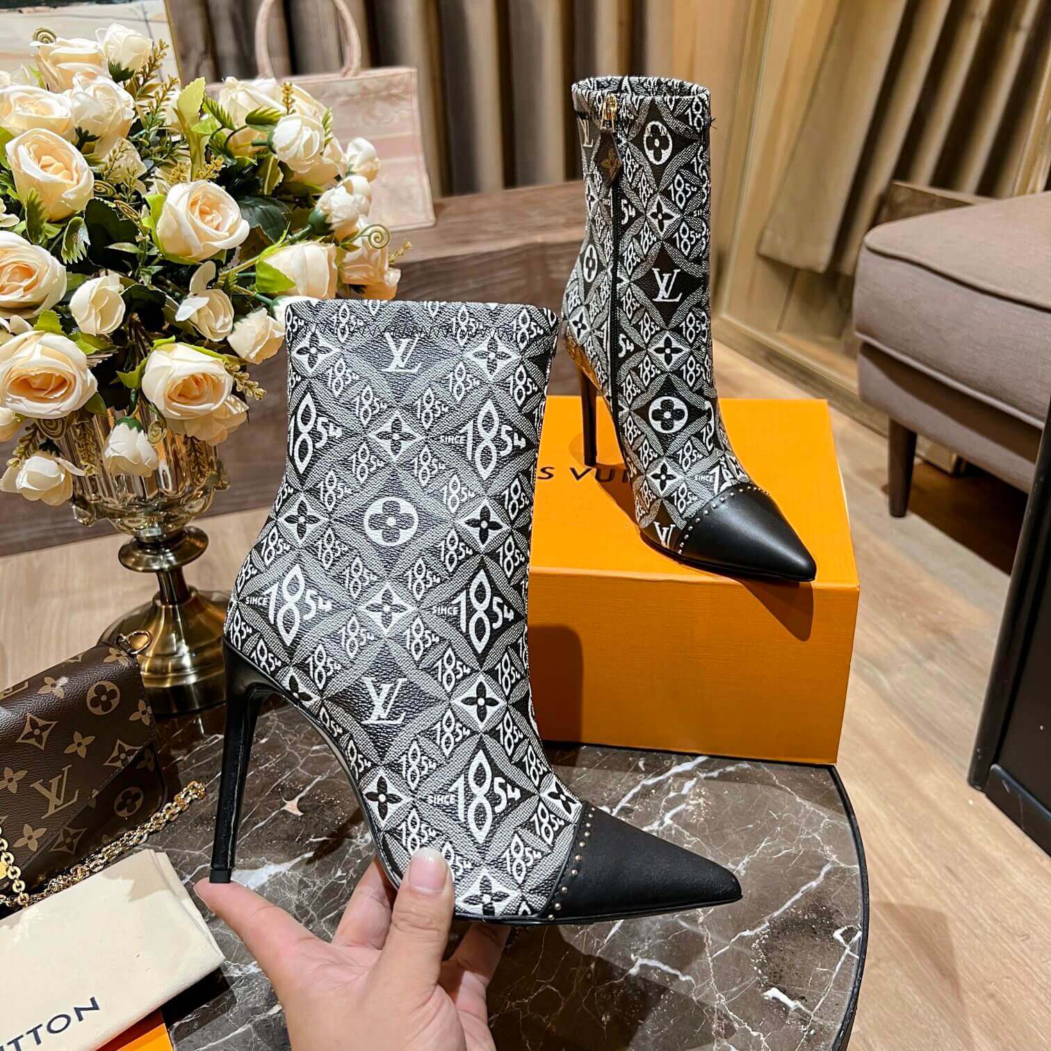 a pair of Louis Vuitton-Inspired Cherrie Ankle Boots – Monogram Noir on a table