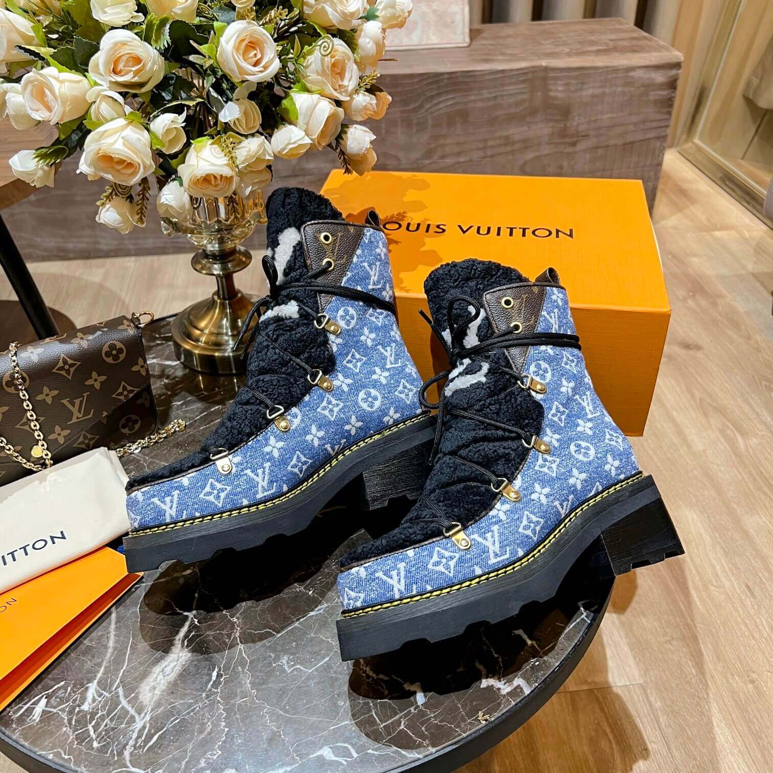 a pair of Louis Vuitton Beaubourg Ankle Boots in a Blue Monogram Denim and Black Shearling on a marble surface