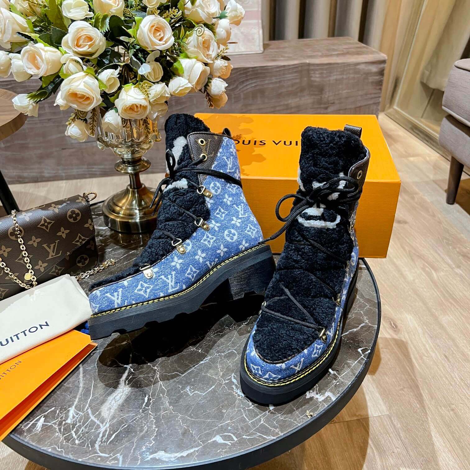 a pair of Louis Vuitton Beaubourg Ankle Boots in a Blue Monogram Denim and Black Shearling on a marble surface