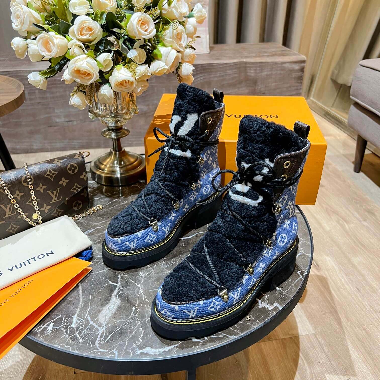 a pair of Louis Vuitton Beaubourg Ankle Boots in a Blue Monogram Denim and Black Shearling on a marble surface