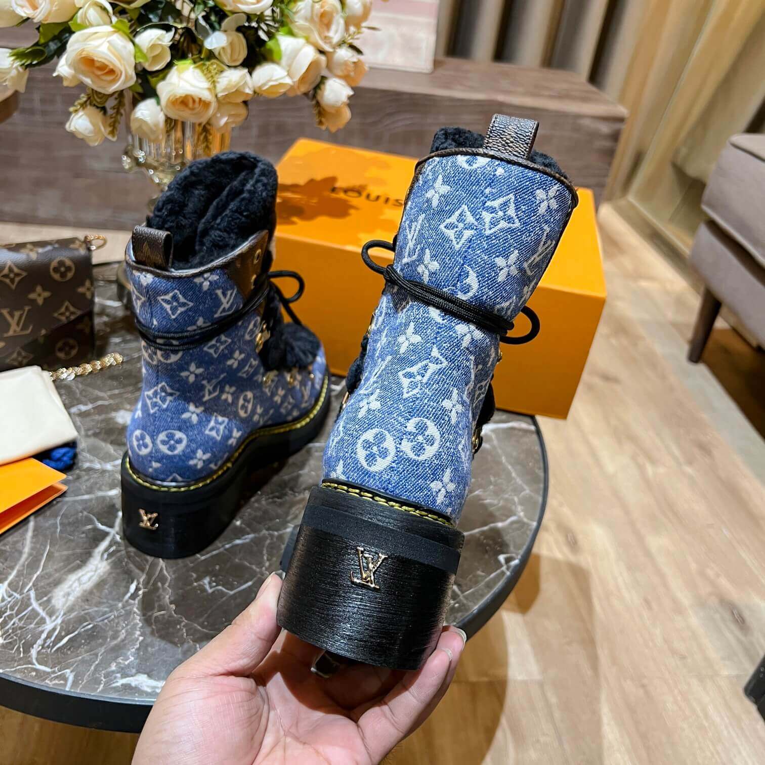 a pair of Louis Vuitton Beaubourg Ankle Boots in a Blue Monogram Denim and Black Shearling on a marble surface