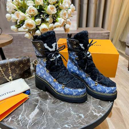 a pair of Louis Vuitton Beaubourg Ankle Boots in a Blue Monogram Denim and Black Shearling on a marble surface