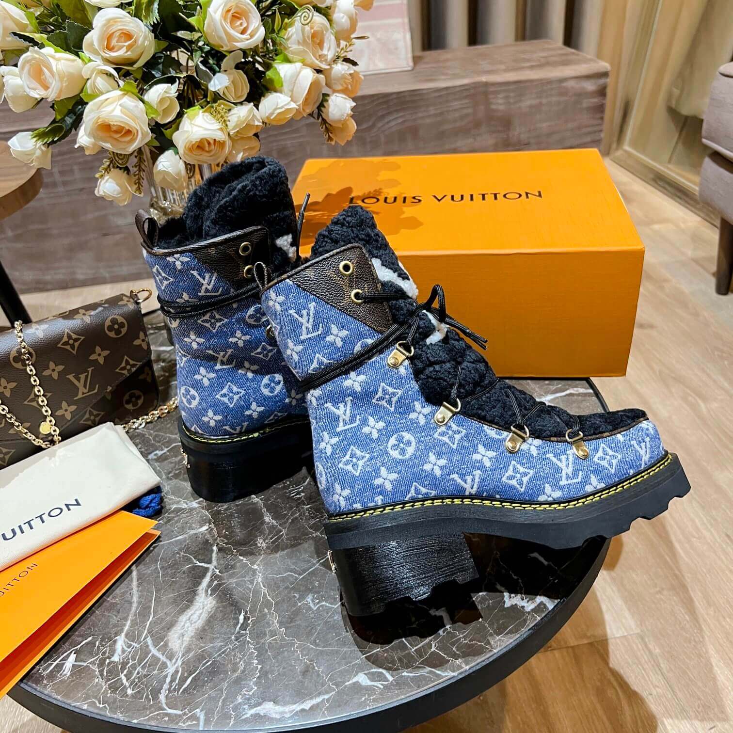 a pair of Louis Vuitton Beaubourg Ankle Boots in a Blue Monogram Denim and Black Shearling on a marble surface