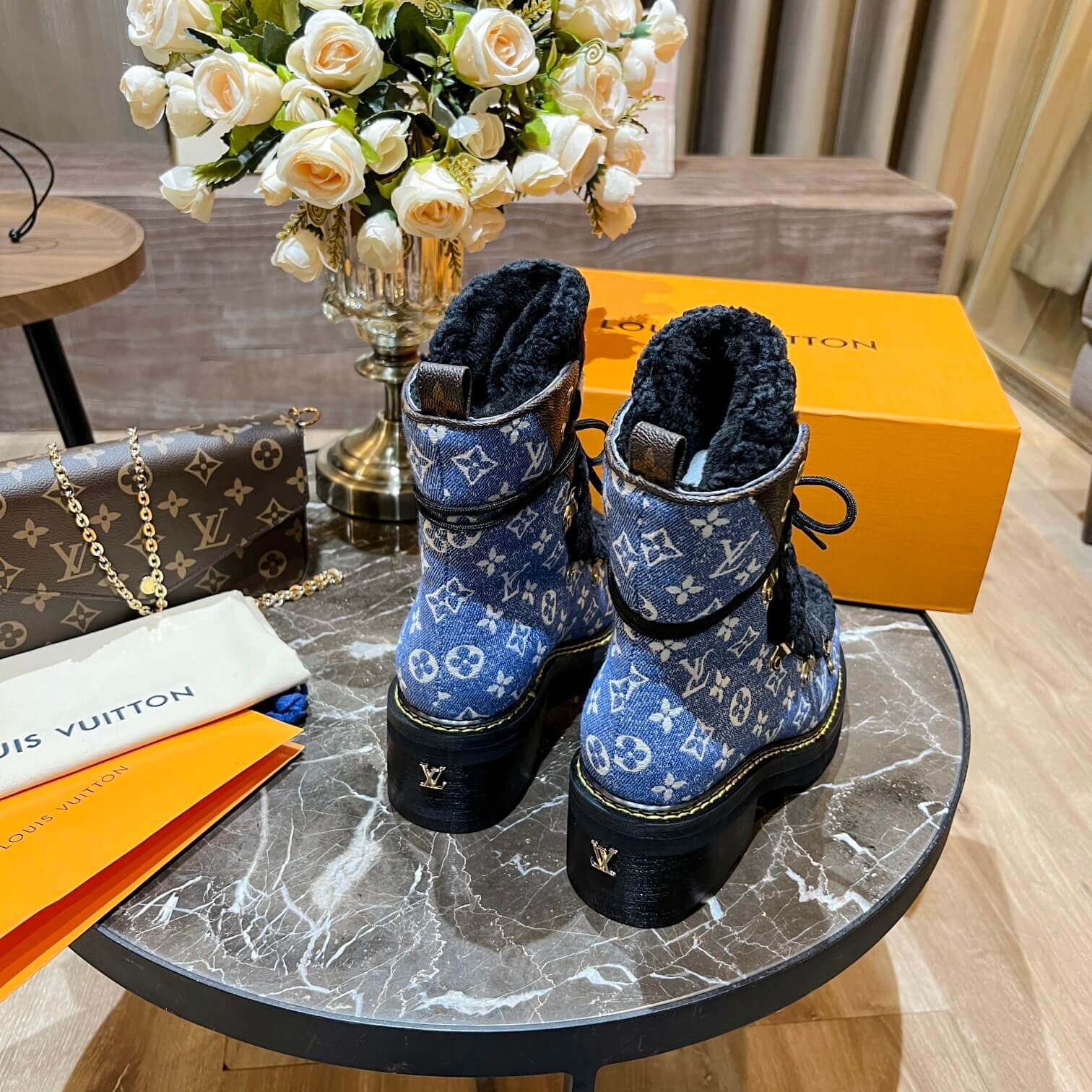 a pair of Louis Vuitton Beaubourg Ankle Boots in a Blue Monogram Denim and Black Shearling on a marble surface
