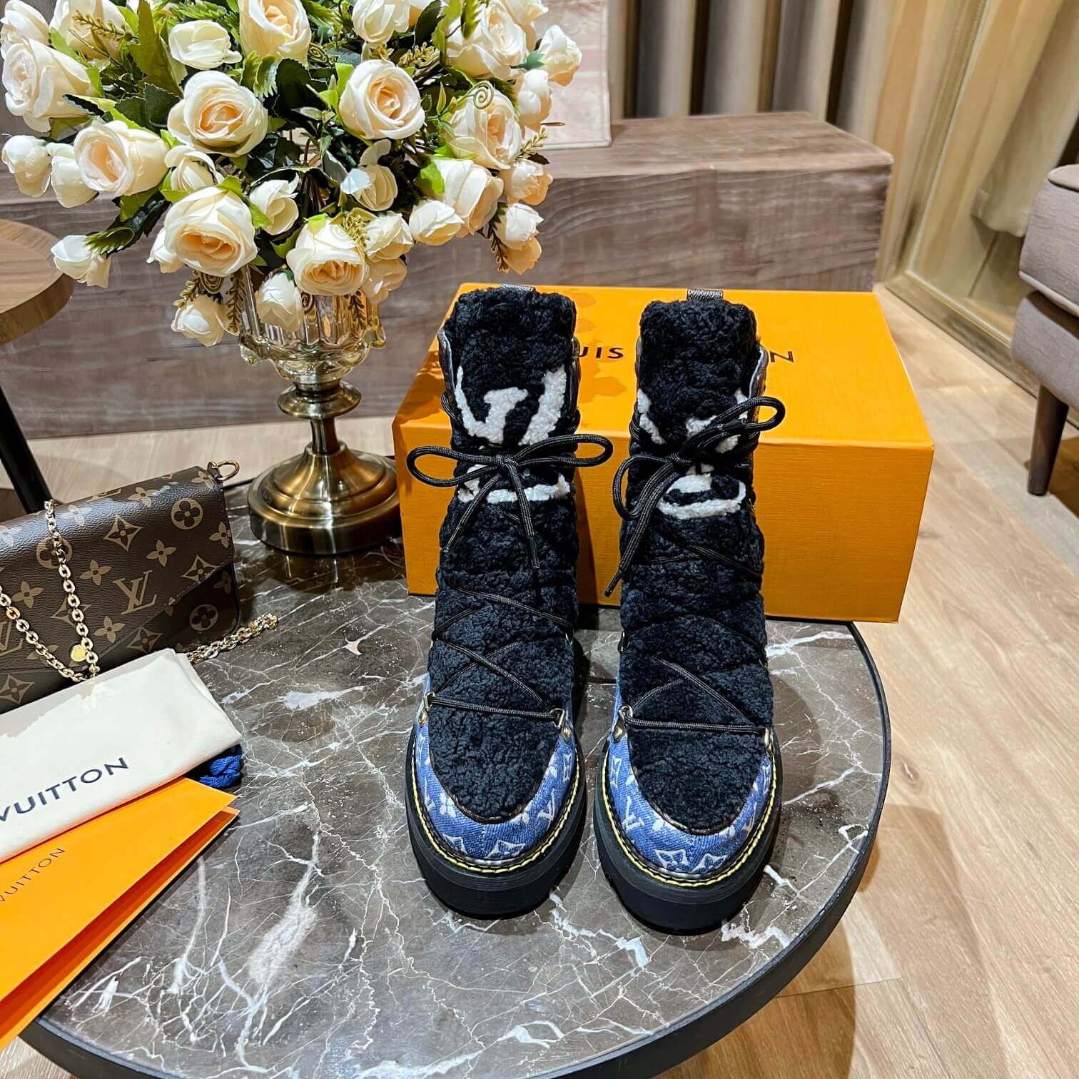 a pair of Louis Vuitton Beaubourg Ankle Boots in a Blue Monogram Denim and Black Shearling on a marble surface
