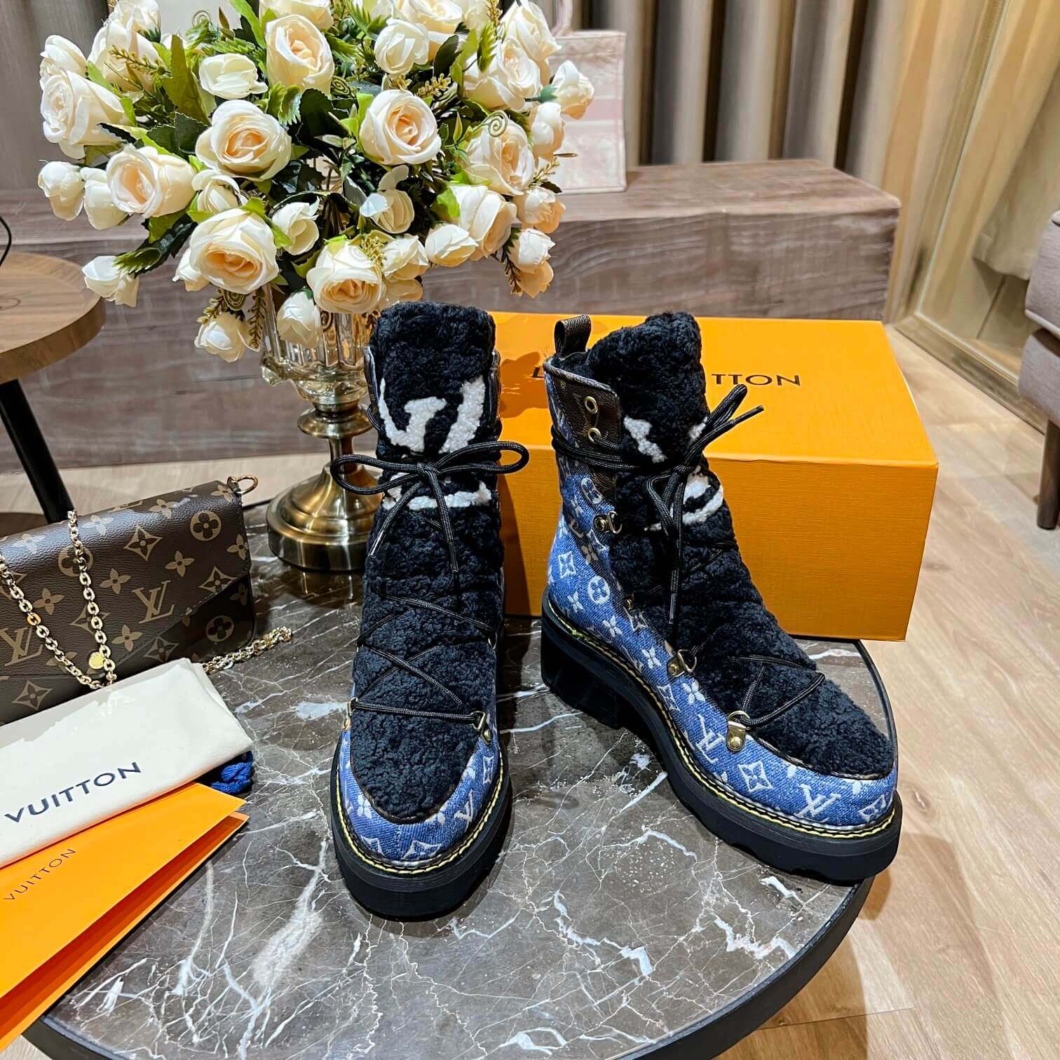 a pair of Louis Vuitton Beaubourg Ankle Boots in a Blue Monogram Denim and Black Shearling on a marble surface