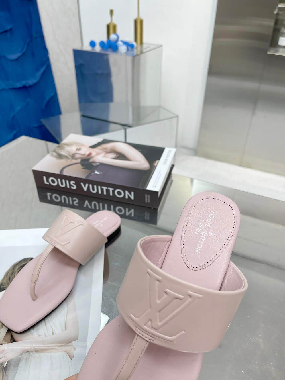 a pair of Louis Vuitton Drapy Flat Thong Sandal in Light Pink on a glass table