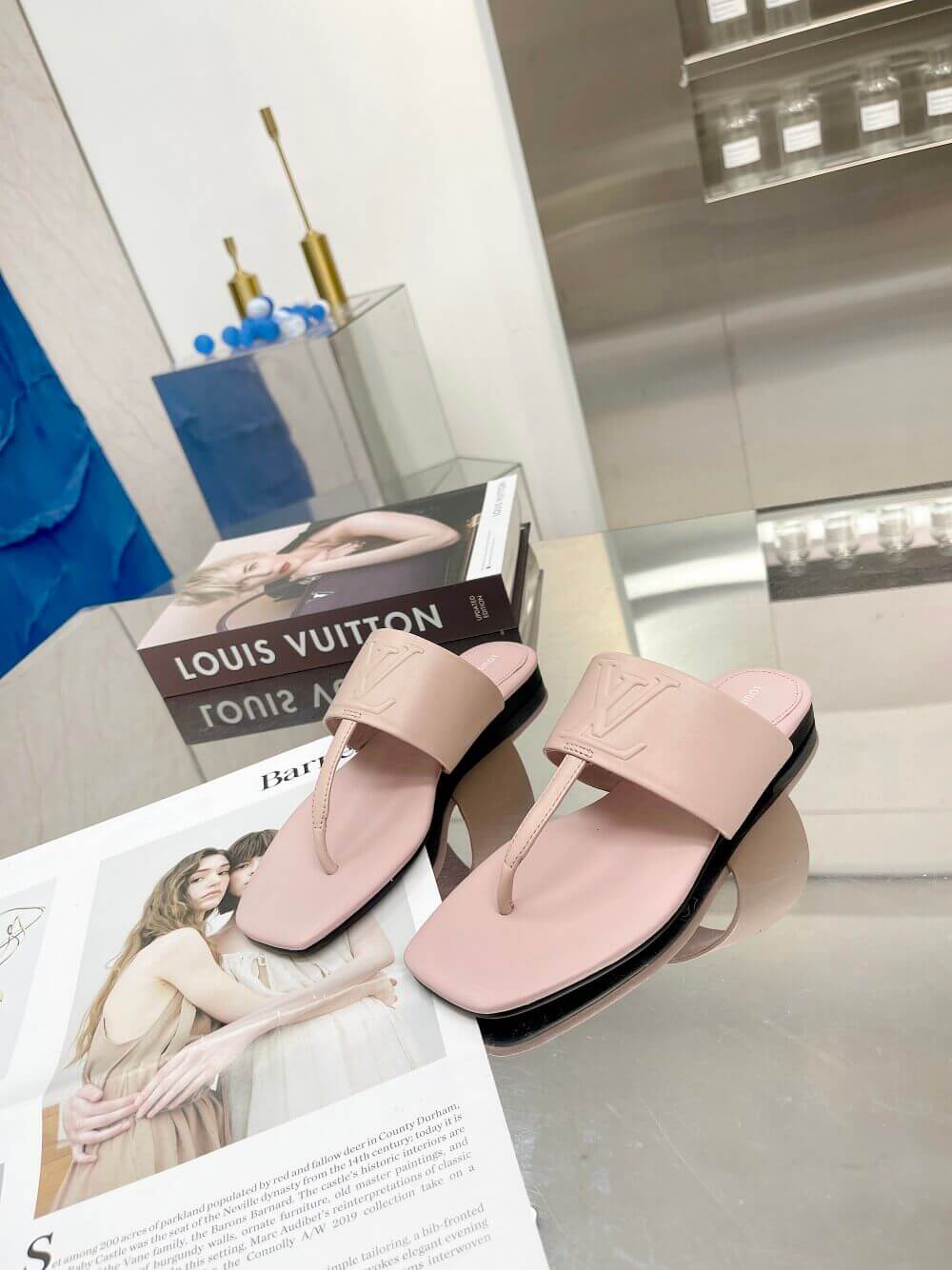 a pair of Louis Vuitton Drapy Flat Thong Sandal in Light Pink on a glass table