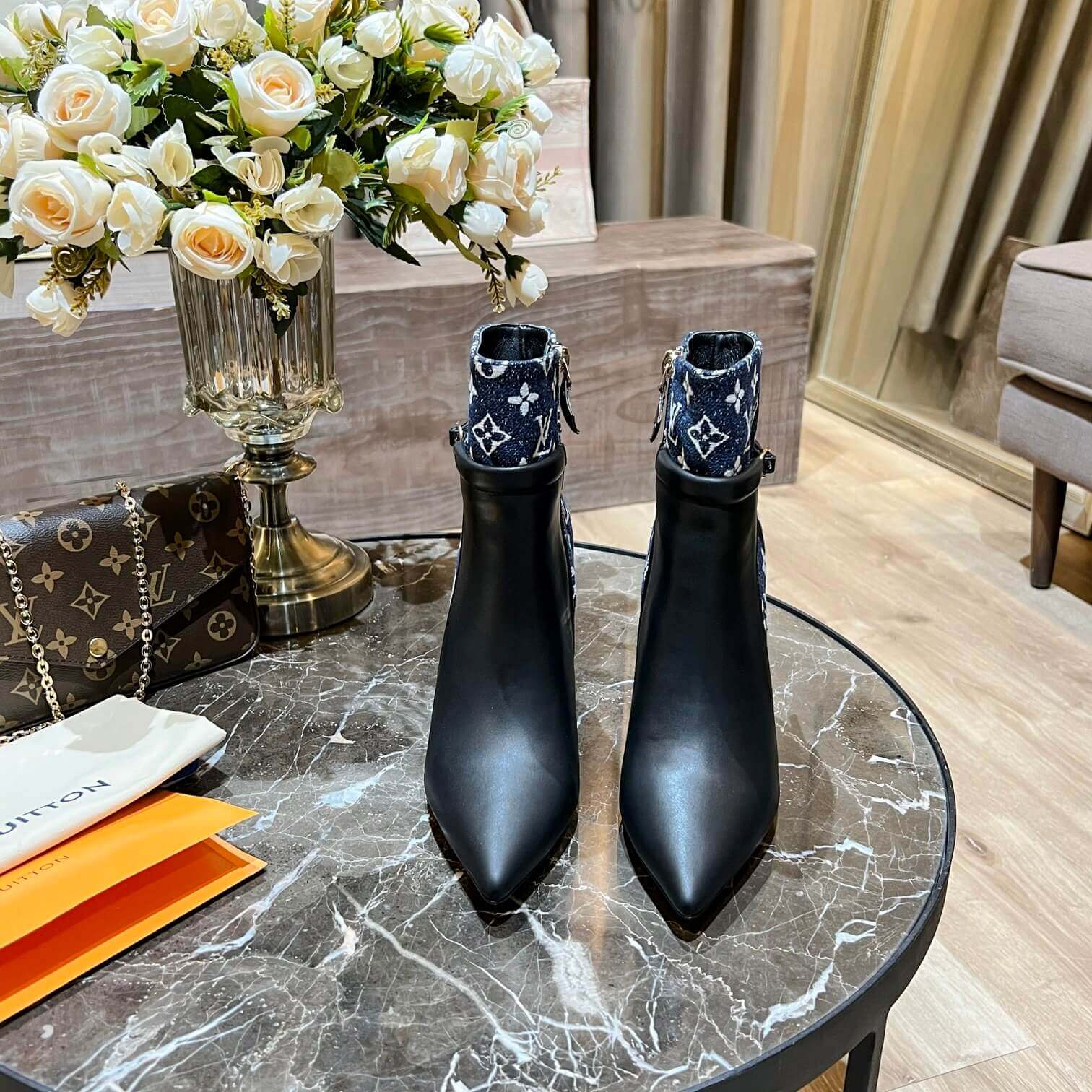 a pair of Louis Vuitton High-Heeled Ankle Boots In Black & Blue Monogram on a marble table