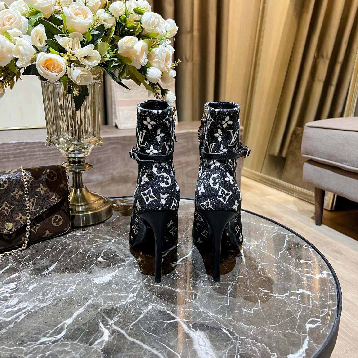 a pair of Louis Vuitton High-Heeled Ankle Boots In Black & Blue Monogram on a marble table