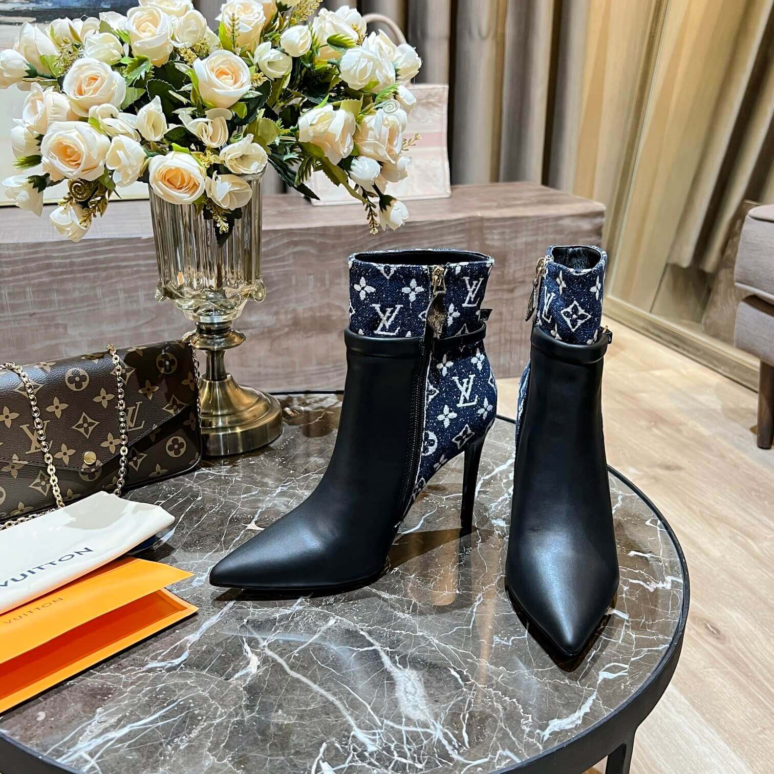 a pair of Louis Vuitton High-Heeled Ankle Boots In Black & Blue Monogram on a marble table