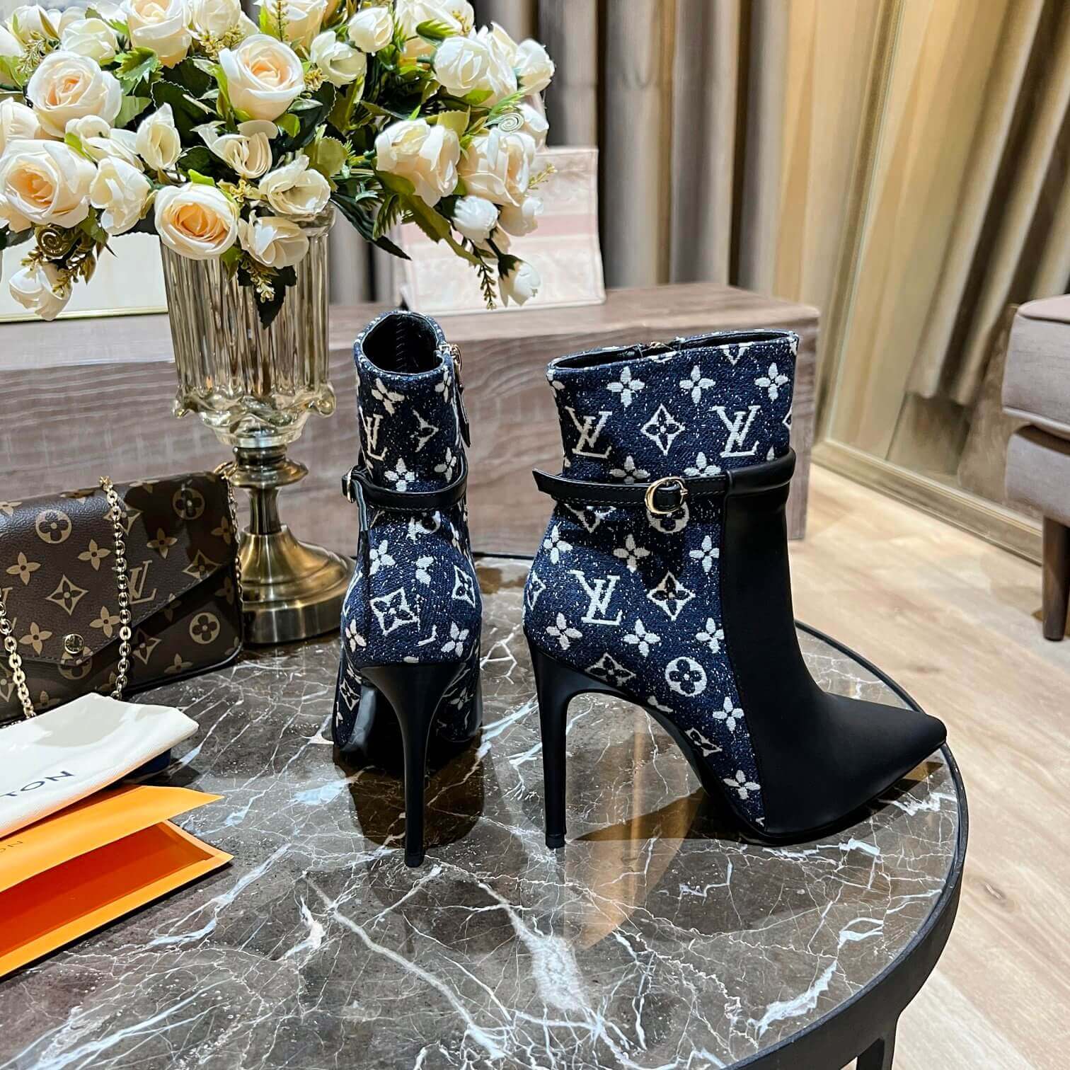 a pair of Louis Vuitton High-Heeled Ankle Boots In Black & Blue Monogram on a marble table