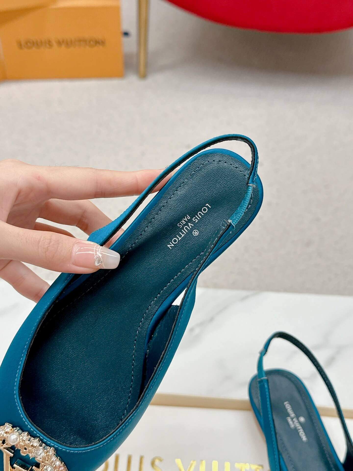 a pair ofLouis Vuitton Madeleine Crystal Slingback –In Teal Blue on a marble table