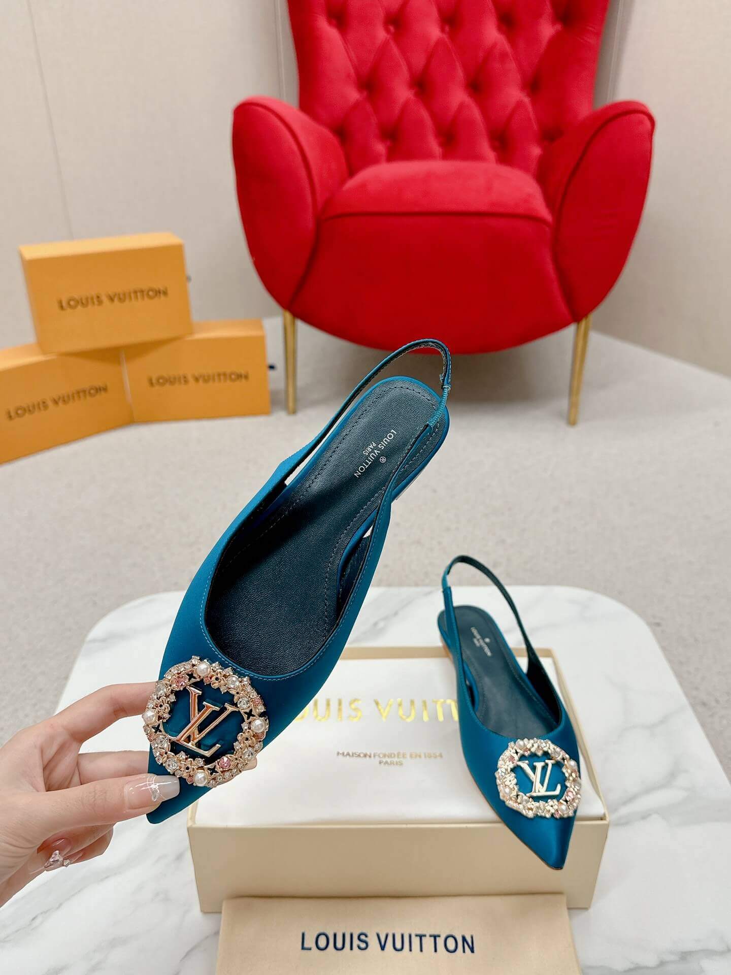 a pair ofLouis Vuitton Madeleine Crystal Slingback –In Teal Blue on a marble table