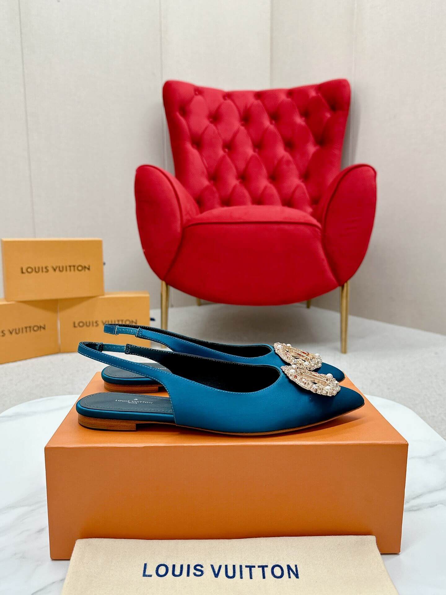 a pair ofLouis Vuitton Madeleine Crystal Slingback –In Teal Blue on a marble table
