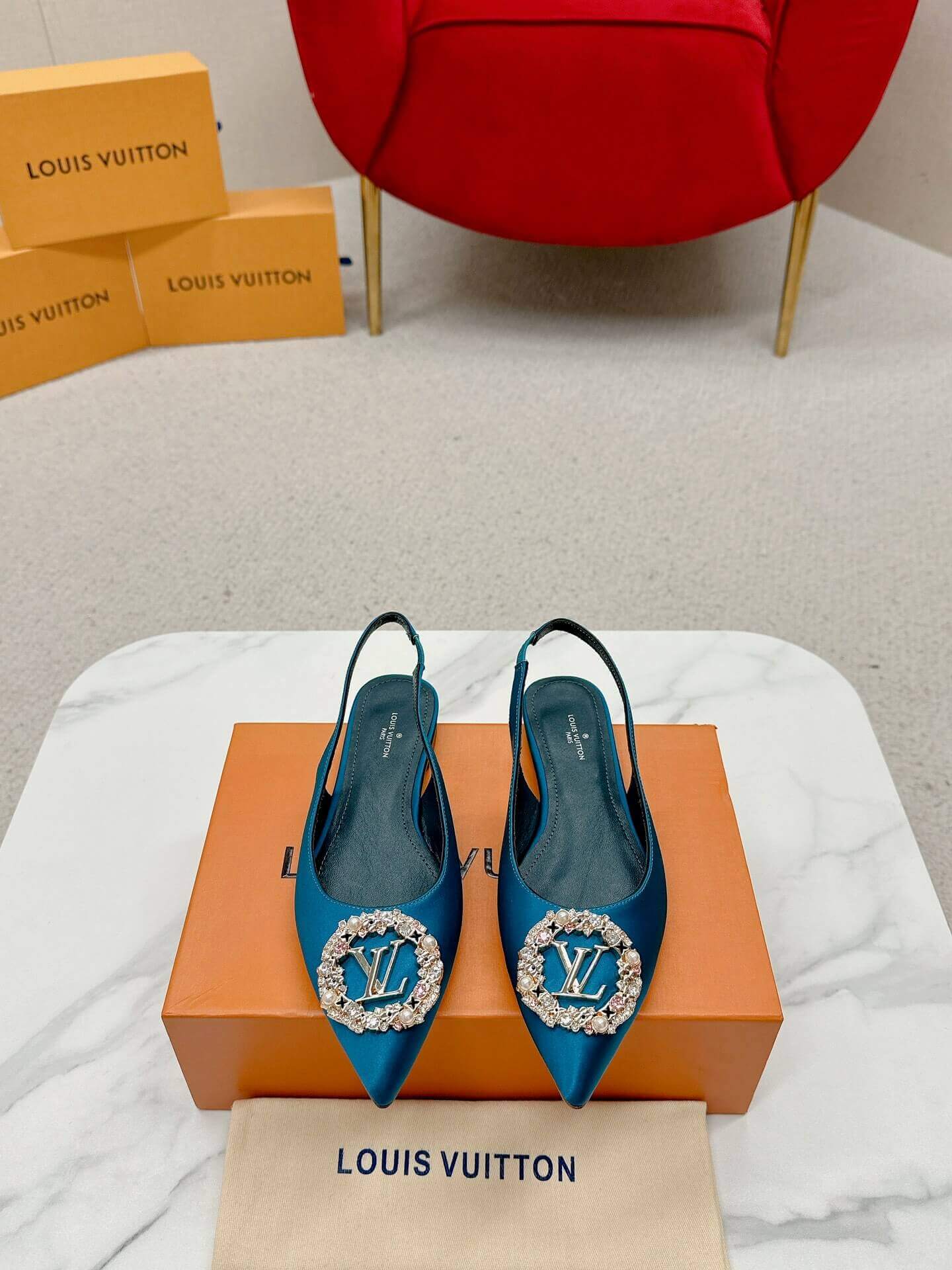 a pair ofLouis Vuitton Madeleine Crystal Slingback –In Teal Blue on a marble table