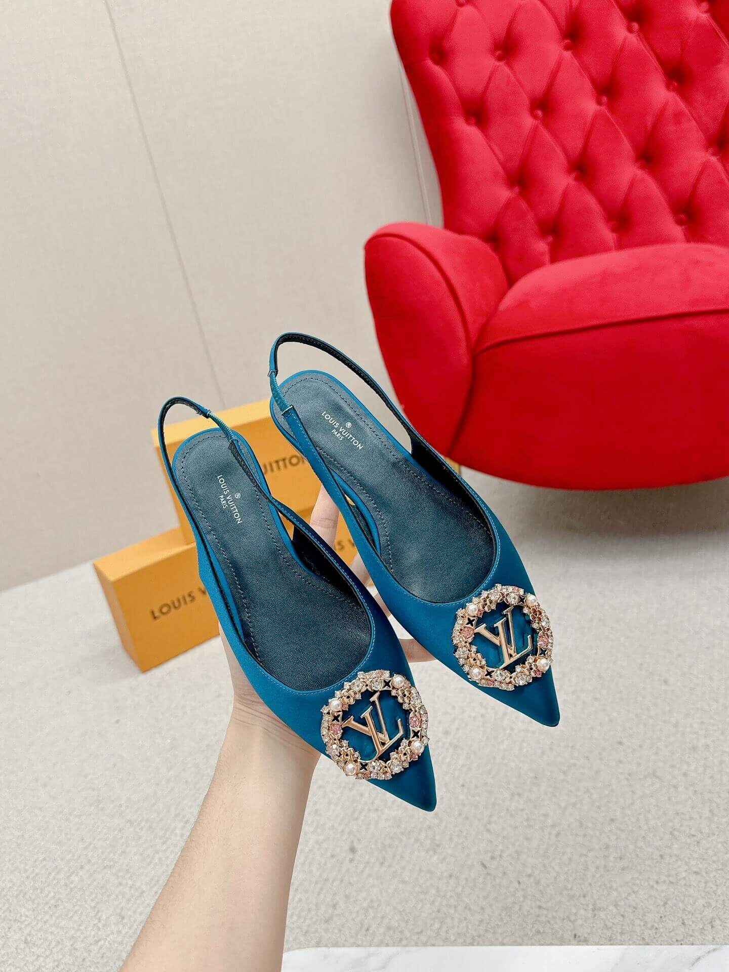a pair ofLouis Vuitton Madeleine Crystal Slingback –In Teal Blue on a marble table