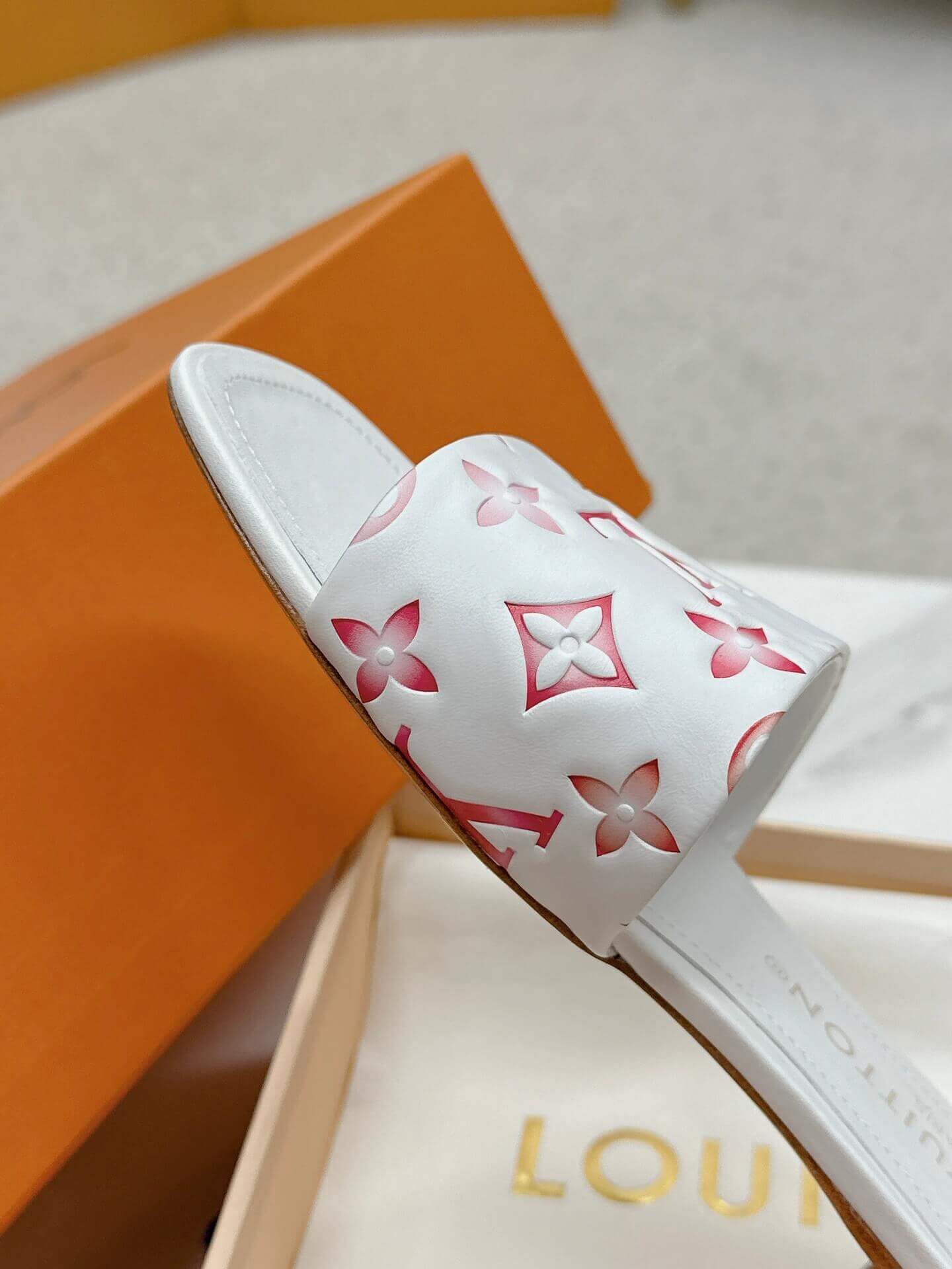 a pair of Louis Vuitton White Monogram Slide Sandals – Pink Edition on a marble surface