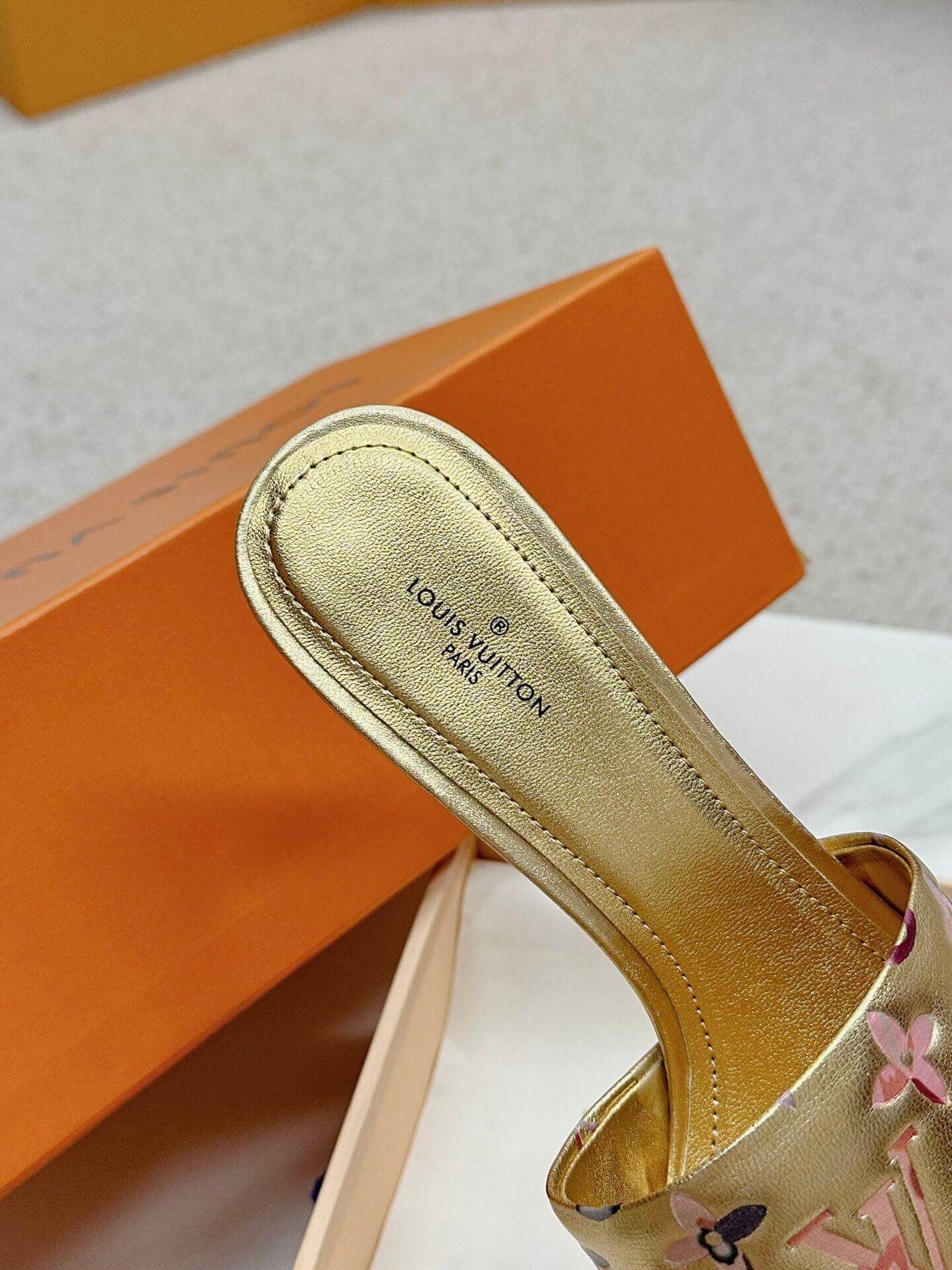 a pair of Louis Vuitton Revival Mule in Gold Monogram-Embossed Lambskin Heel on a marble surface