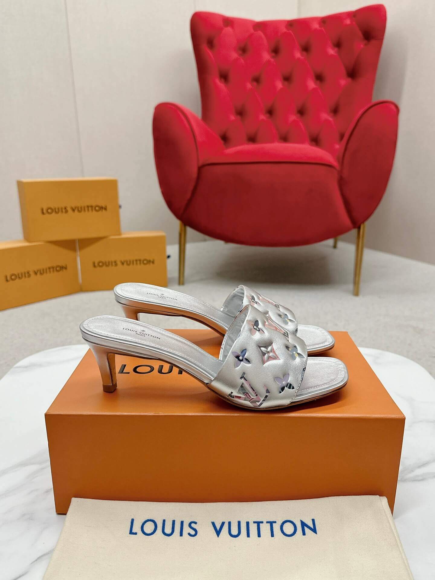 a pair of Louis Vuitton Revival Mule in Silver Metallic Monogram‑Embossed Heel on a marble surface