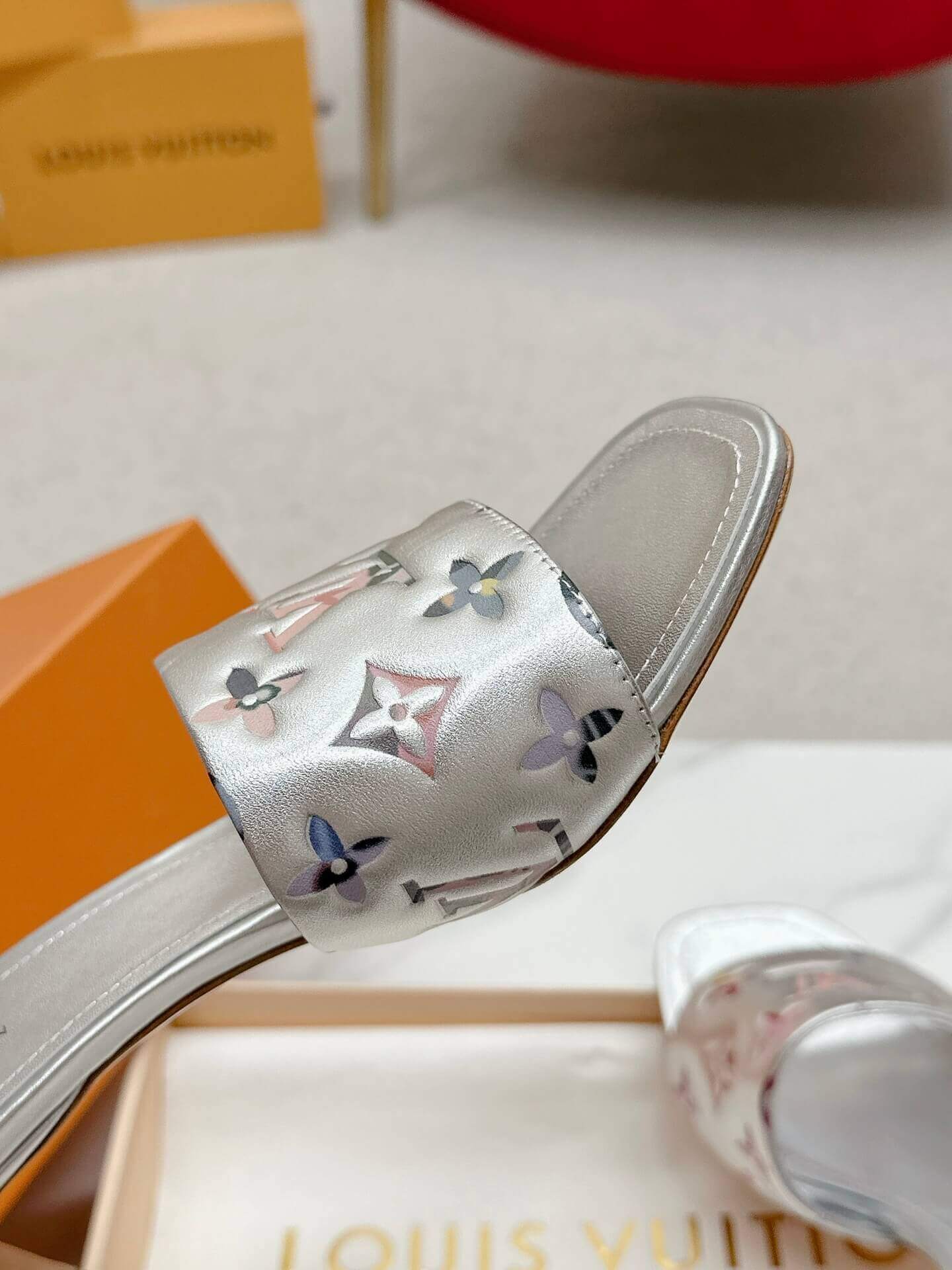 a pair of Louis Vuitton Revival Mule in Silver Metallic Monogram‑Embossed Heel on a marble surface