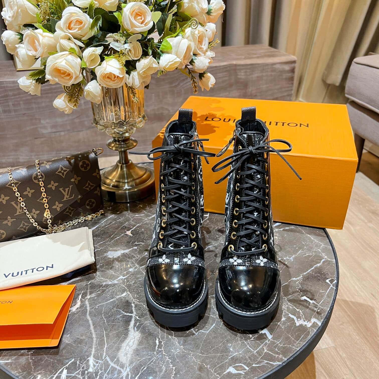 a pair of Louis Vuitton Star Trail Ankle Boots (Black Monogramon a marble table