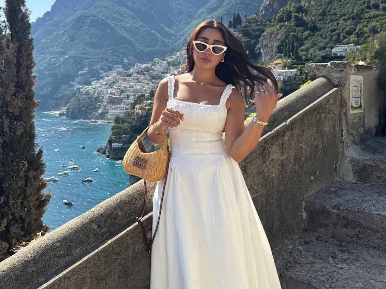 Elegant white linen maxi dress paired with trendy cat-eye sunglasses and a mini straw handbag for a luxury vacation outfit.
